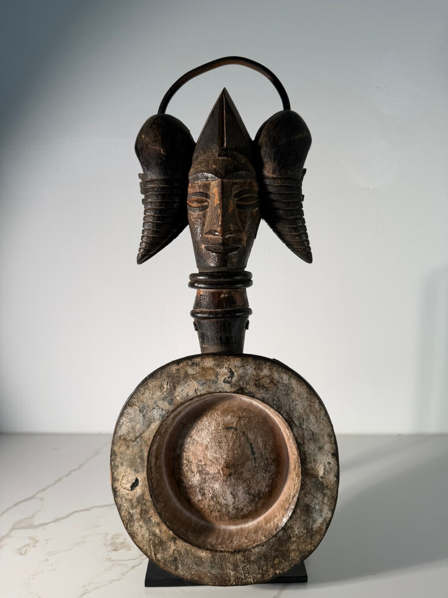Igbo Okwa Nzu Cosmetic Bowl with Female Head Finial, Nigeria, 19th/20th Century: Known as an Okwa Nzu or cosmetic bowl, originating from Nigeria. The object is carved primarily from dark wood and features a highly stylized female head finial mounted on a long neck. The head is cha