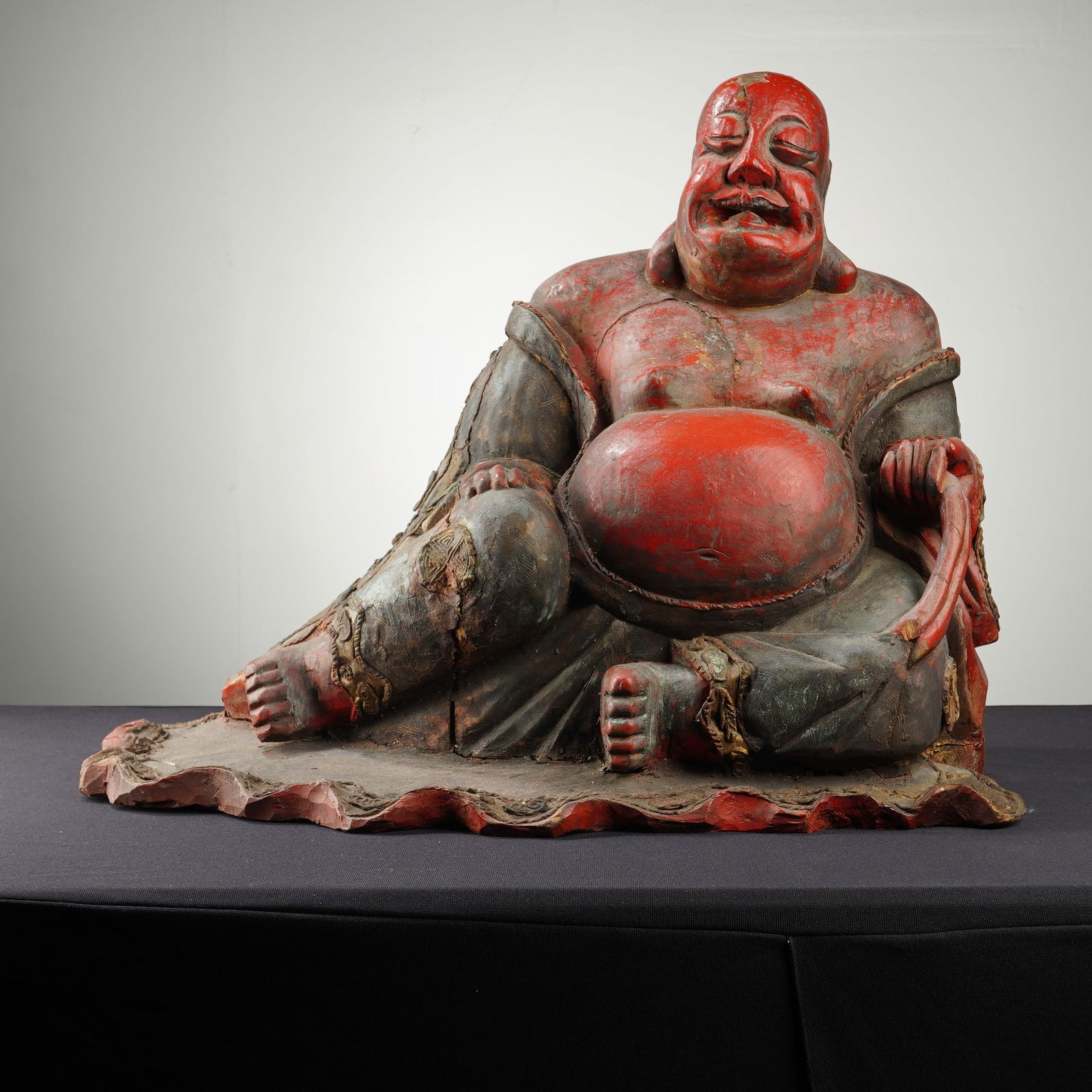 Chinese Carved Wood and Lacquer Laughing Buddha Sculpture: This large Chinese carved wood sculpture of the Laughing Buddha is executed in solid wood with a polychrome and lacquer finish. The figure is depicted in a reclined pose, with a prominent exposed bell