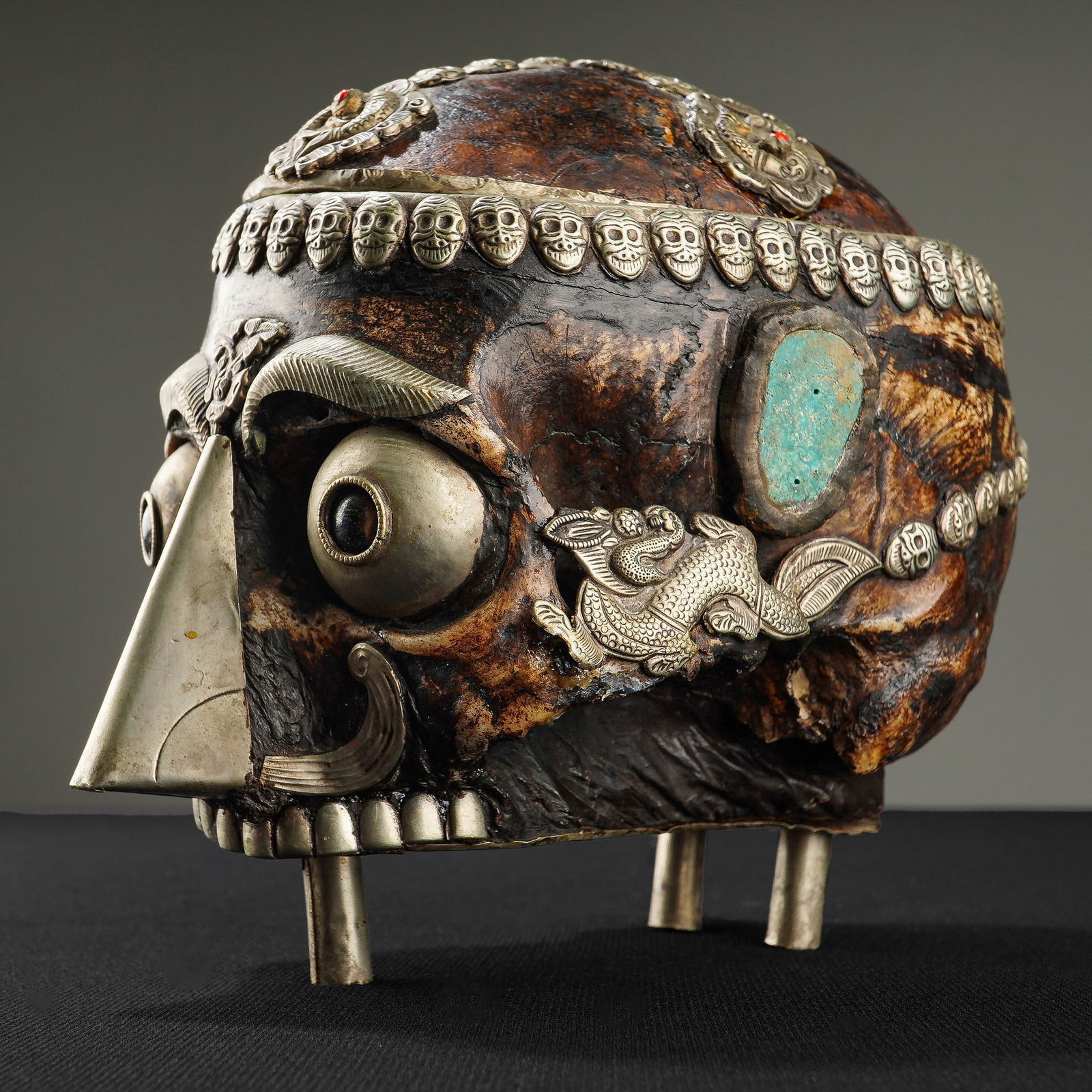 Tibetan Carved Bovine Bone Skull-Form Reliquary Box: The vessel is constructed with a hinged domed lid and is supported by three short metallic peg feet. The exterior bone surface displays a dark, polished patina and is embellished with metallic decorat