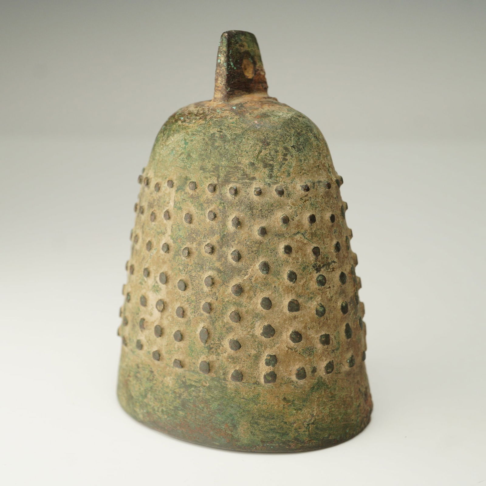 Chinese Archaic Small Bronze Bell: A small Chinese archaic bronze bell of conical form, the surface adorned with a uniform pattern of raised dot bosses arranged in horizontal pattern. A pierced suspension lug surmounts the top,