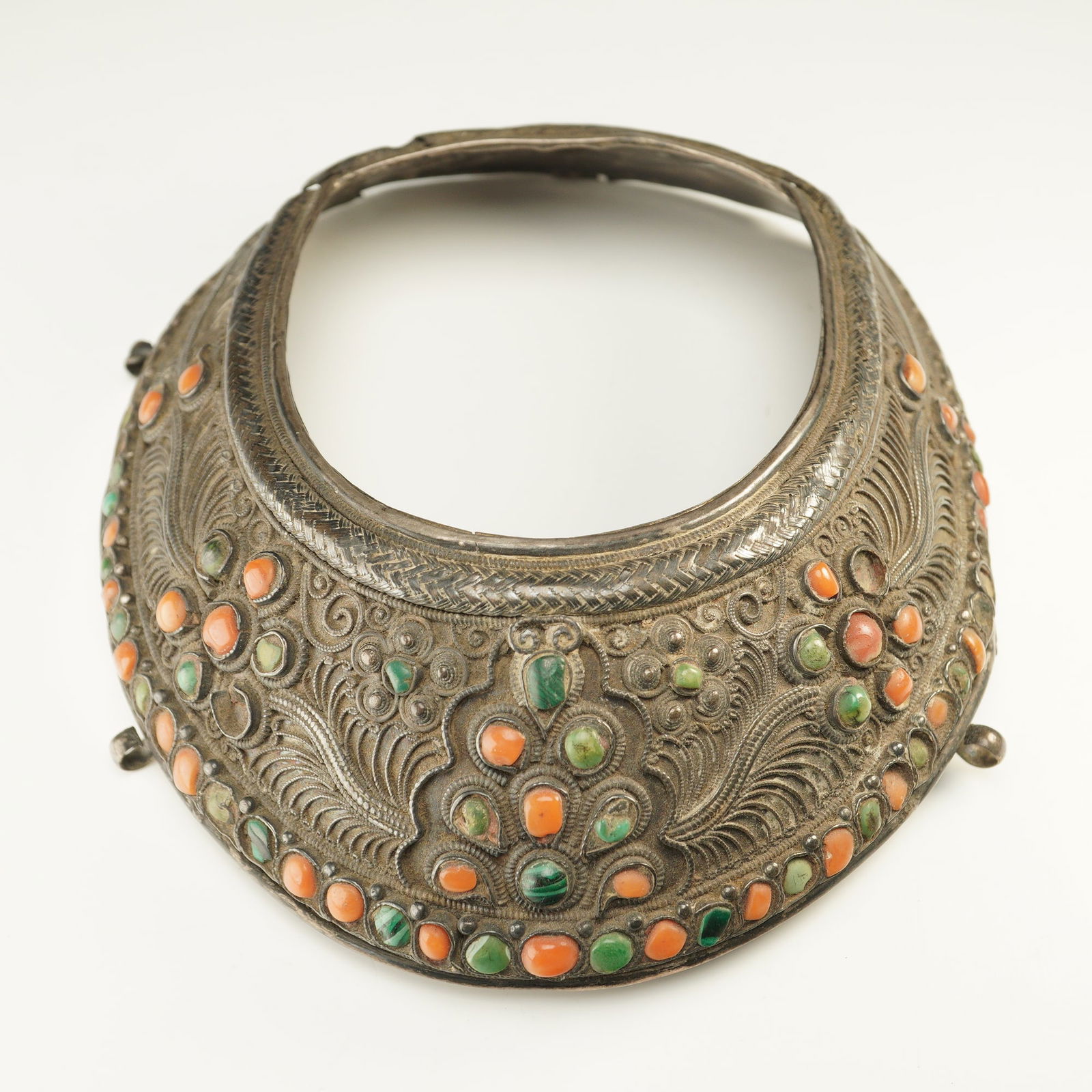 Mongolian Silver Headdress with Coral and Turquoise: A Mongolian silver headdress of domed crescent form, elaborately adorned with raised filigree scrollwork and intricate chased motifs. The surface is set with an arrangement of polished coral and