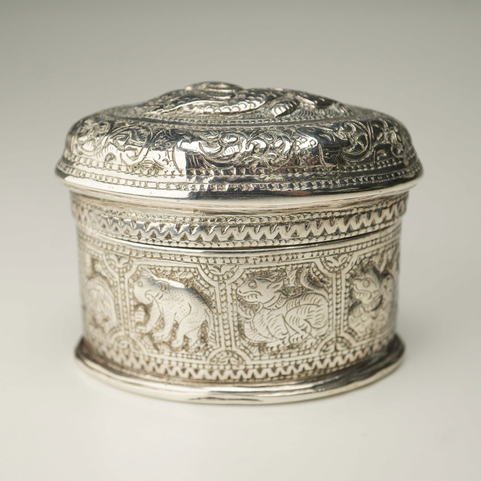 Burmese Silver Oblong Covered Box with Zodiac Animals: Burmese silver small covered box of oblong form, meticulously worked with detail. The exterior panels adorned with zodiac animals framed within geometric borders. The domed lid is decorated with a