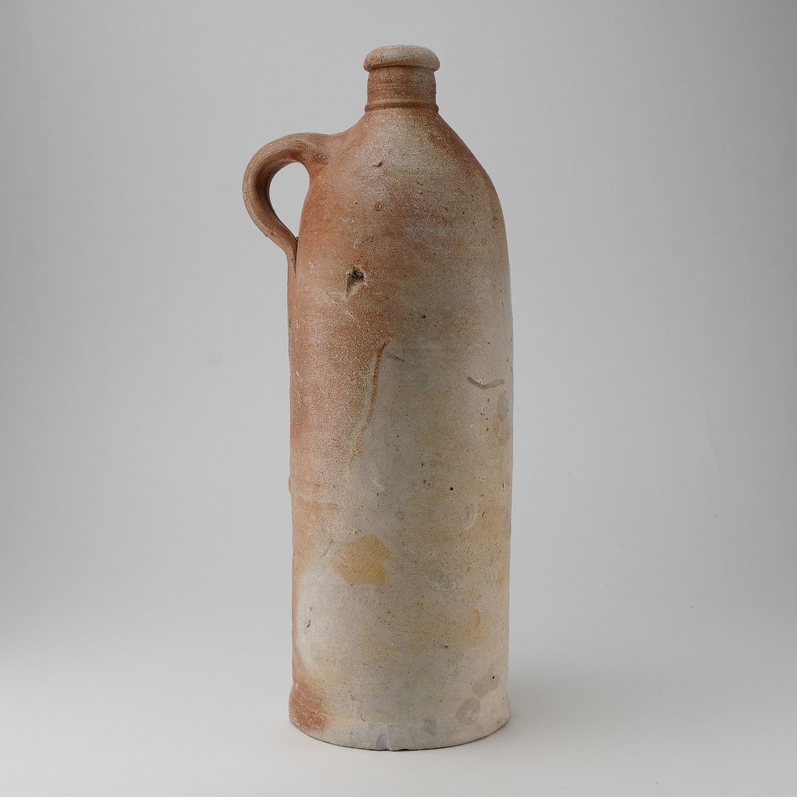Antique Ming Dynasty Salt Glazed Stoneware Jug: Antique cylindrical stoneware jug featuring a salt glaze exterior. The jug has a narrow neck and a thickened, rounded lip showing interior chipping and visible surface cracks. The body transitions fro
