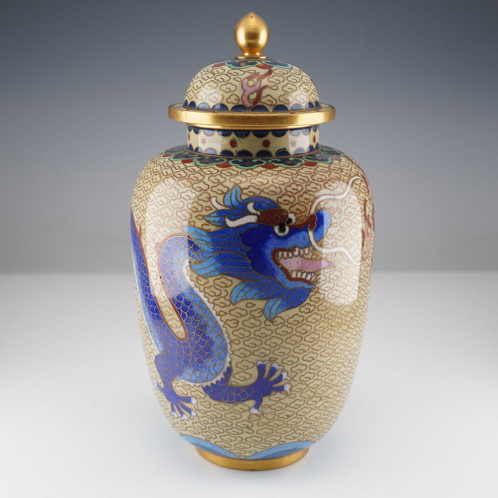A Chinese Cloisonne Dragon Lidded Vase: A Chinese cloisonne enamel and brass border lidded vase, featuring a bulbous body and a domed lid topped with a spherical gilt finial. The primary decoration consists of two prominently rendered blue