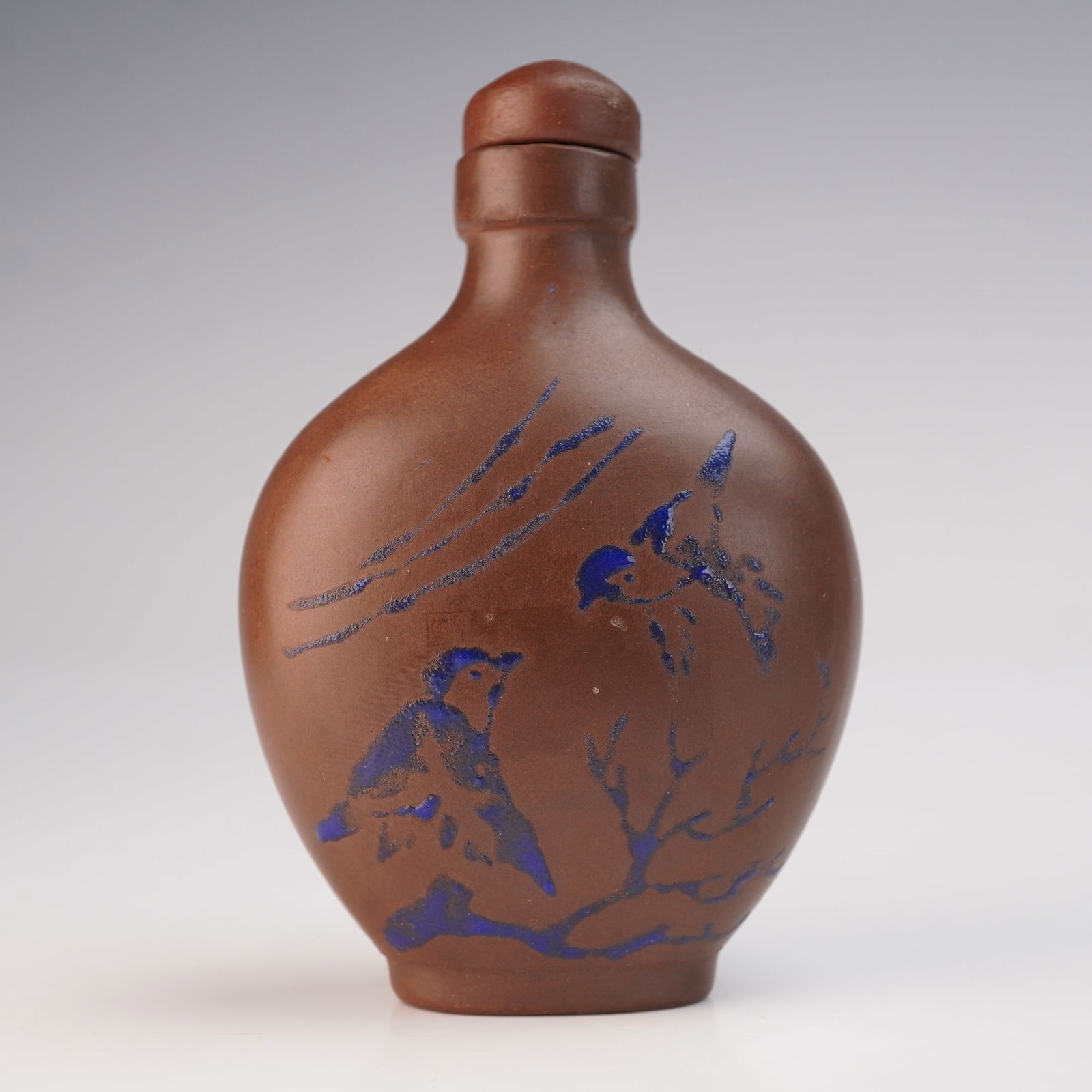 Chinese Yixing Pottery Enameled Snuff Bottle: A Yixing pottery enameled snuff bottle, formed in a classic flattened oval silhouette and accompanied by its spoon. The reddish-brown body is delicately adorned with blue enamel decoration depicting s