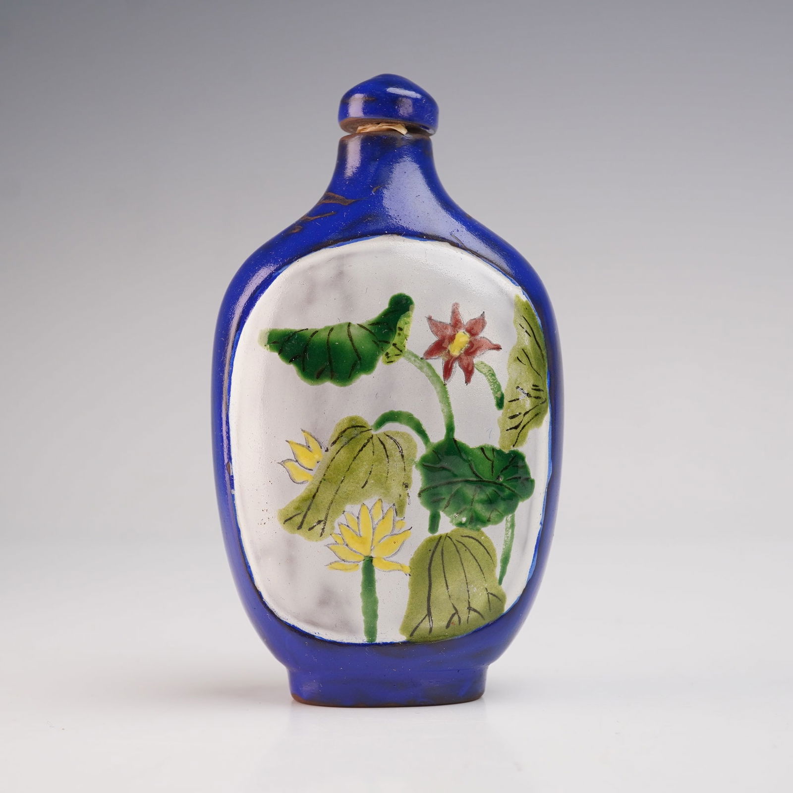 Chinese Yixing Pottery Enameled Snuff Bottle with Floral Panels: A Yixing pottery snuff bottle, its surface richly enameled and accentuated with polychrome floral panels. The body is finished in a deep cobalt blue glaze, framing white reserves that display delicate