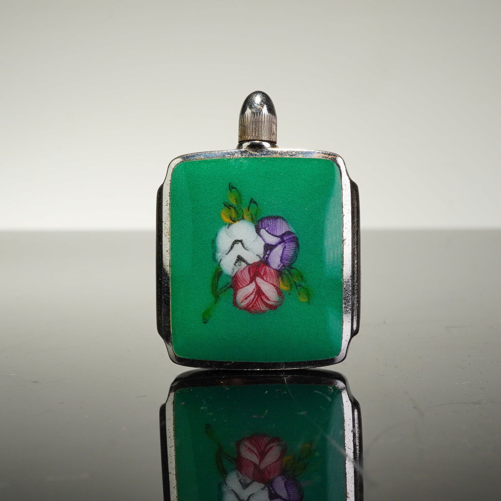Sterling Silver and Enamel Floral Snuff Bottle: A sterling silver and enamel snuff bottle featuring a square body with stepped sides. The front is decorated with a panel of vibrant green enamel centered by a hand-painted floral bouquet in white, pu