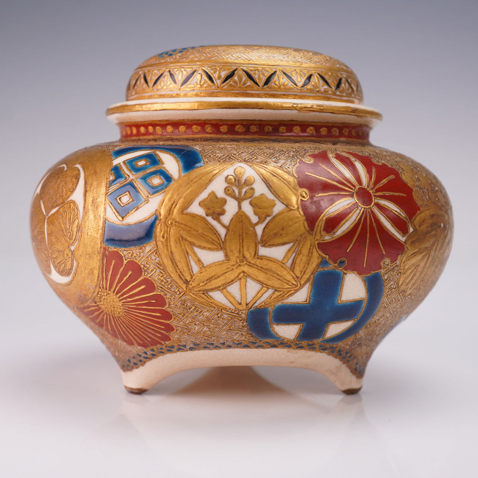 2pc Japanese Satsuma Mon Design Koro Censer Burner with Lid: The form features a rounded body supported by four short feet, topped with a fitted domed lid. The exterior surfaces are embellished with multiple mon (Japanese family emblems) rendered in red, blue,