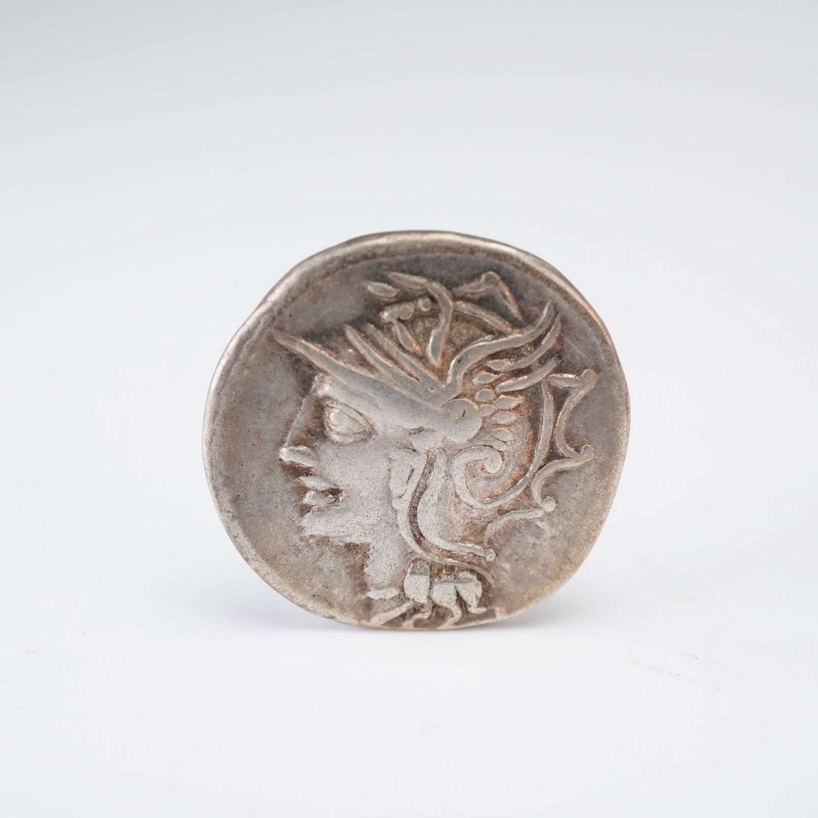 Roman Republic Silver Denarious Coin: Attributed to moneyer Lucius Appuleius Saturninus, featuring on the obverse a helmeted female head facing right, adorned with wing-like embellishments and framed by stylized hair details. The reverse