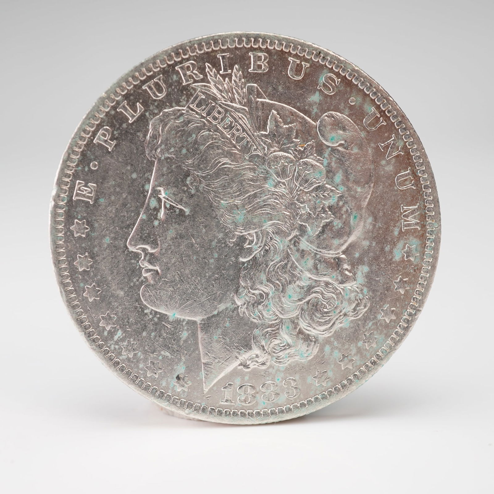 1883-O Morgan Silver Dollar: An 1883-O Morgan Silver Dollar struck at the New Orleans Mint. The obverse displays the classical profile of Liberty wearing a Phrygian cap adorned with wheat and cotton, symbolizing agricultural pros