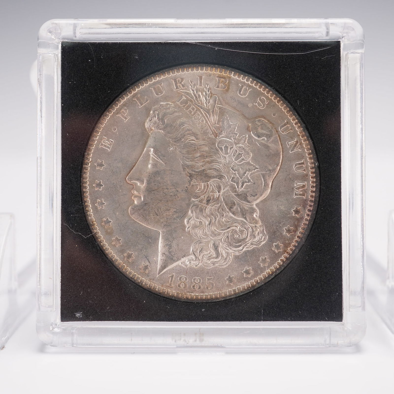 1885-O Morgan Silver Dollar: Struck at the New Orleans Mint. The obverse features the profile of Liberty facing left, wearing a Phrygian cap adorned with wheat and cotton, encircled by thirteen stars, the motto E PLURIBUS UNUM, a