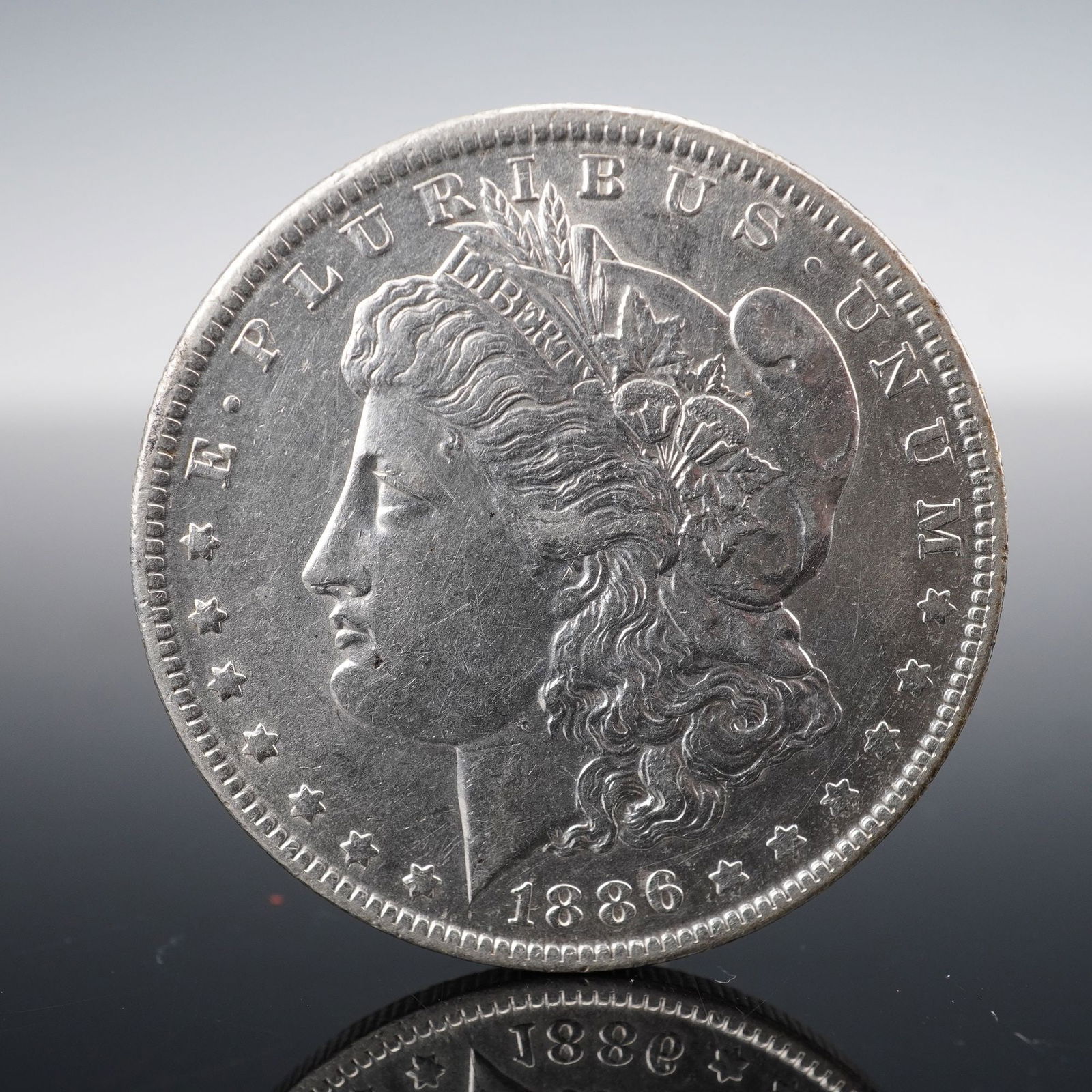 1886-O Morgan Silver Dollar Coin: Minted in New Orleans. The obverse features the profile of Liberty facing left, adorned with a Phrygian cap and surrounded by thirteen stars, the date, and the inscription E PLURIBUS UNUM. The reverse