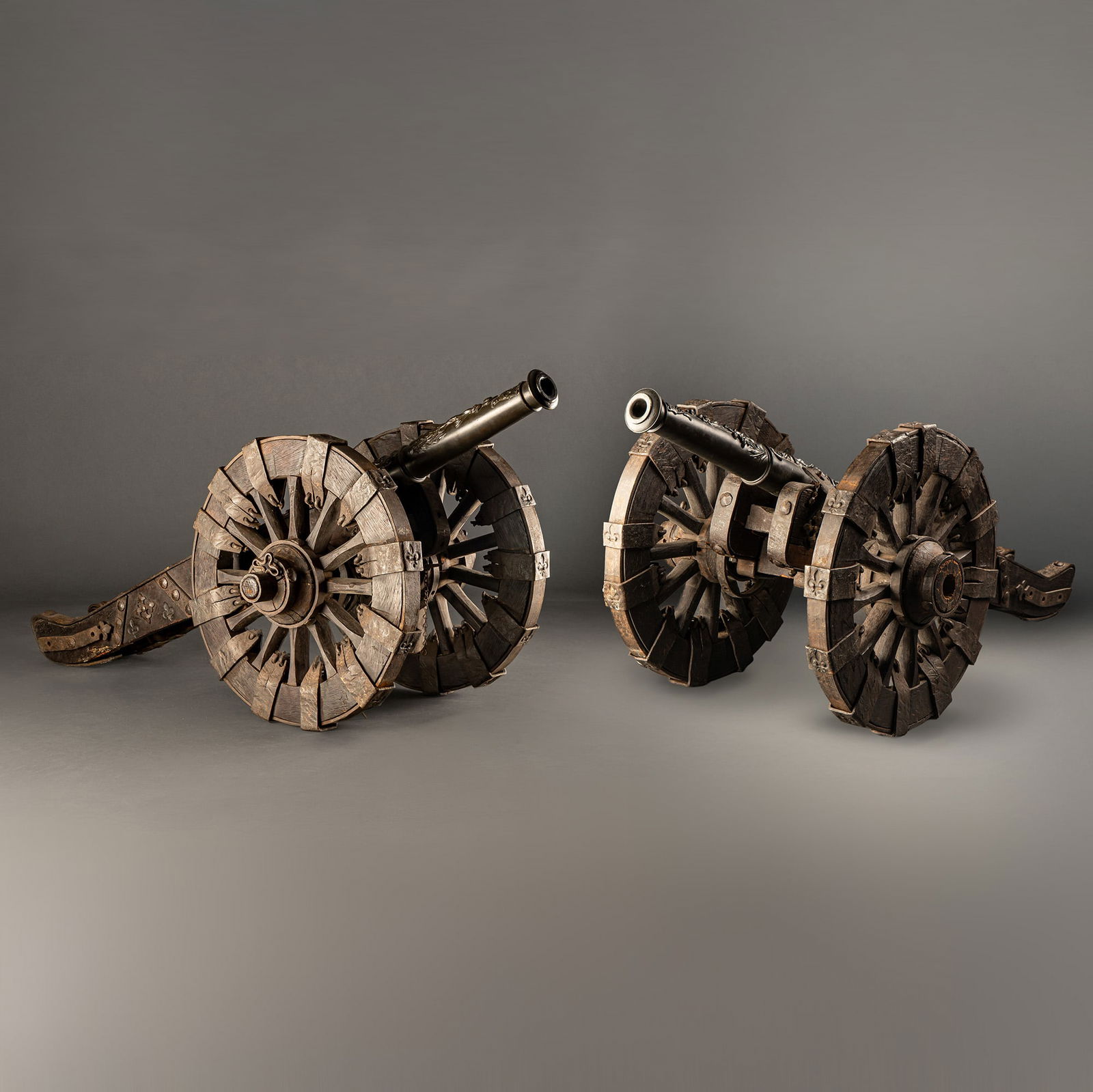 Pair of 19th Century French Military Bronze Signal Cannons: Two bronze cannons mounted on wooden carriages with spoked wheels, origin and date undetermined. The barrels feature intricate reliefs of classical figures, showcasing exceptional detail in the bronze
