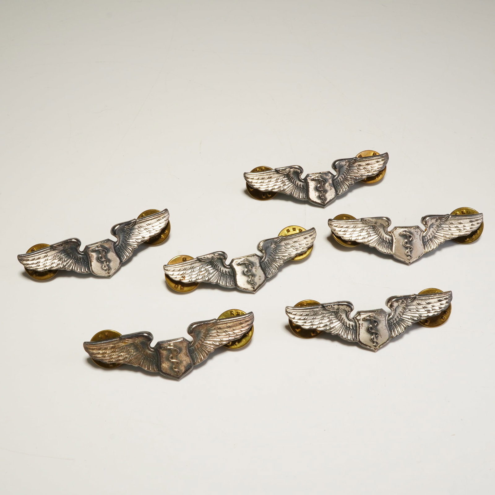 6pc 1/20 Silver Filled U.S. Army Air Force Flight Surgeon Badges: A group of six Vanguard U.S. Army Air Force Flight Surgeon badges crafted from 1/20 silver filled metal and features a central shield embossed with a caduceus flanked by outstretched wings. The revers