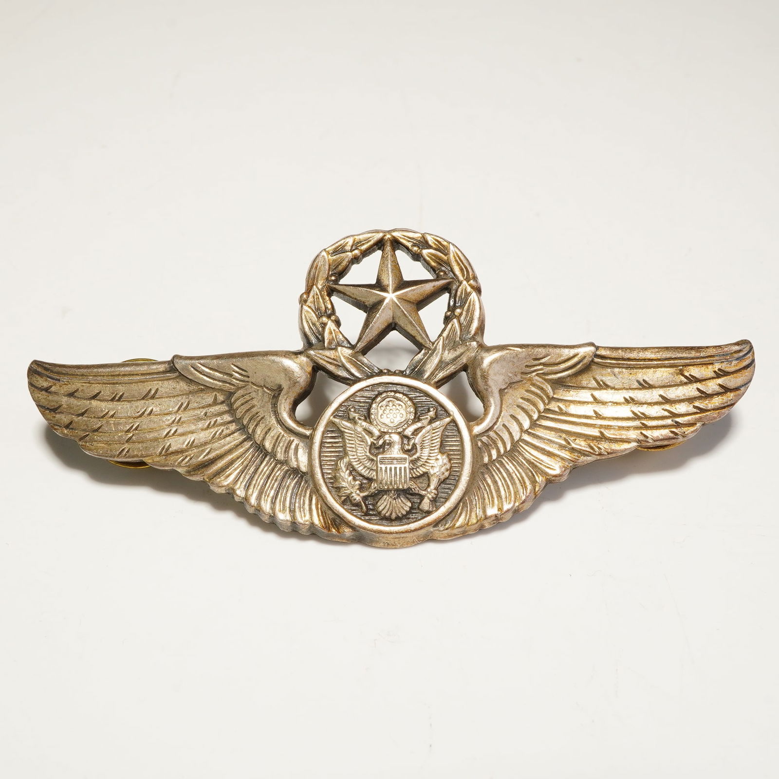 N.S. Meyer Sterling Silver U.S. Air Force Chief Aircrew Member Wings Badge: This badge features a central circular medallion depicting the Great Seal of the United States, flanked by outspread feathered wings. The design is surmounted by a five-pointed star enclosed within a