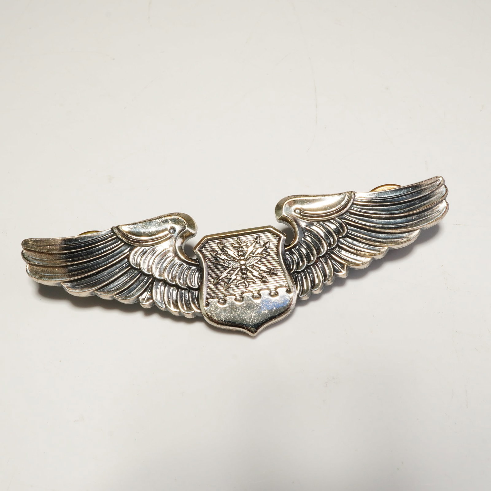 N.S. Meyer Sterling U.S. Air Force Navigator Observer Wings Badge: A sterling silver U.S. Air Force Navigator/Observer wings badge produced by N.S. Meyer. The insignia consists of outspread feathered wings flanking a central shield that features wings and burst of ar