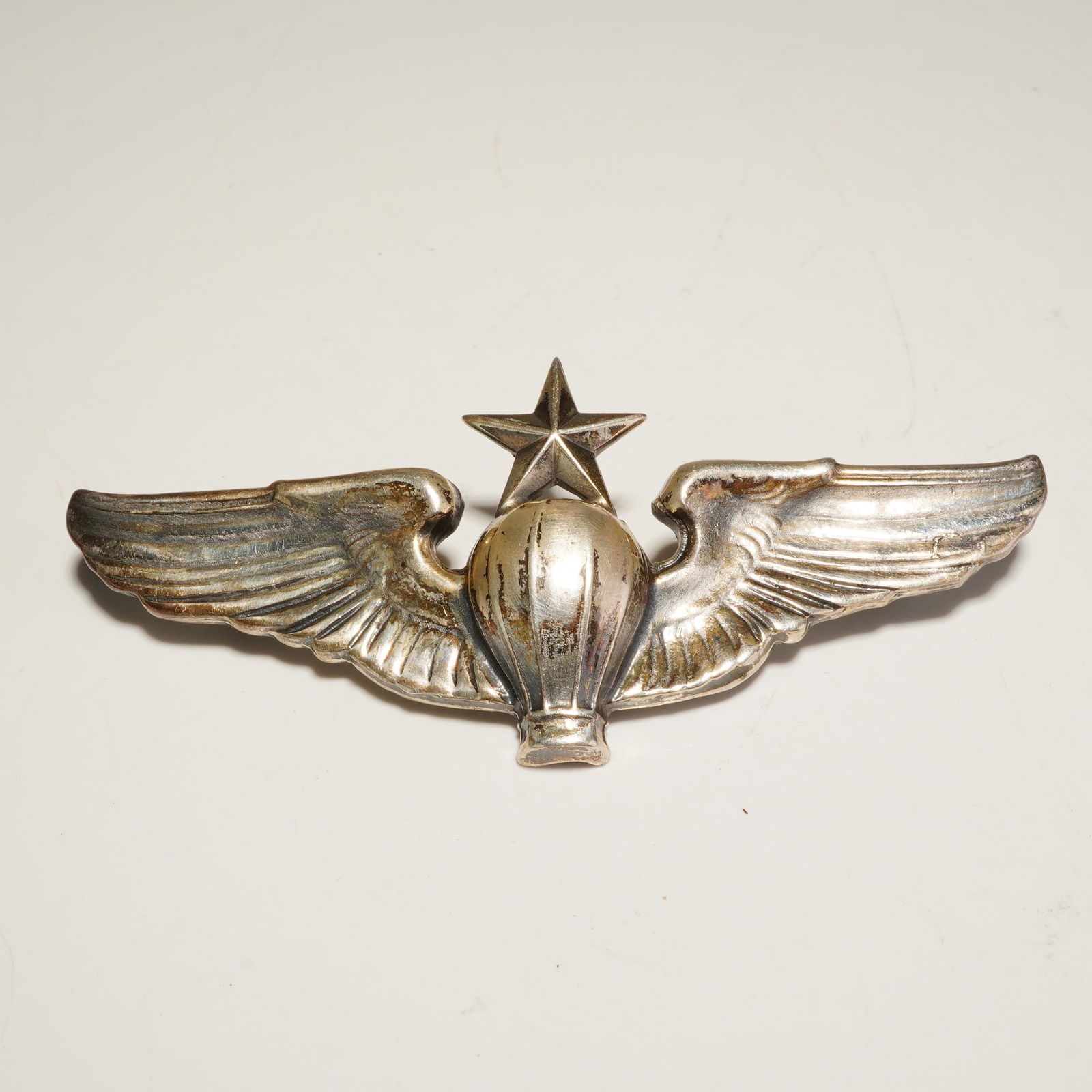 N.S. Meyer Sterling U.S. Army Air Force Senior Balloon Pilot Badge Pin: This N.S. Meyer sterling silver U.S. Army Air Force Senior Balloon Pilot badge pin features a central balloon envelope topped with a five-pointed star and flanked by two outstretched wings. The insign