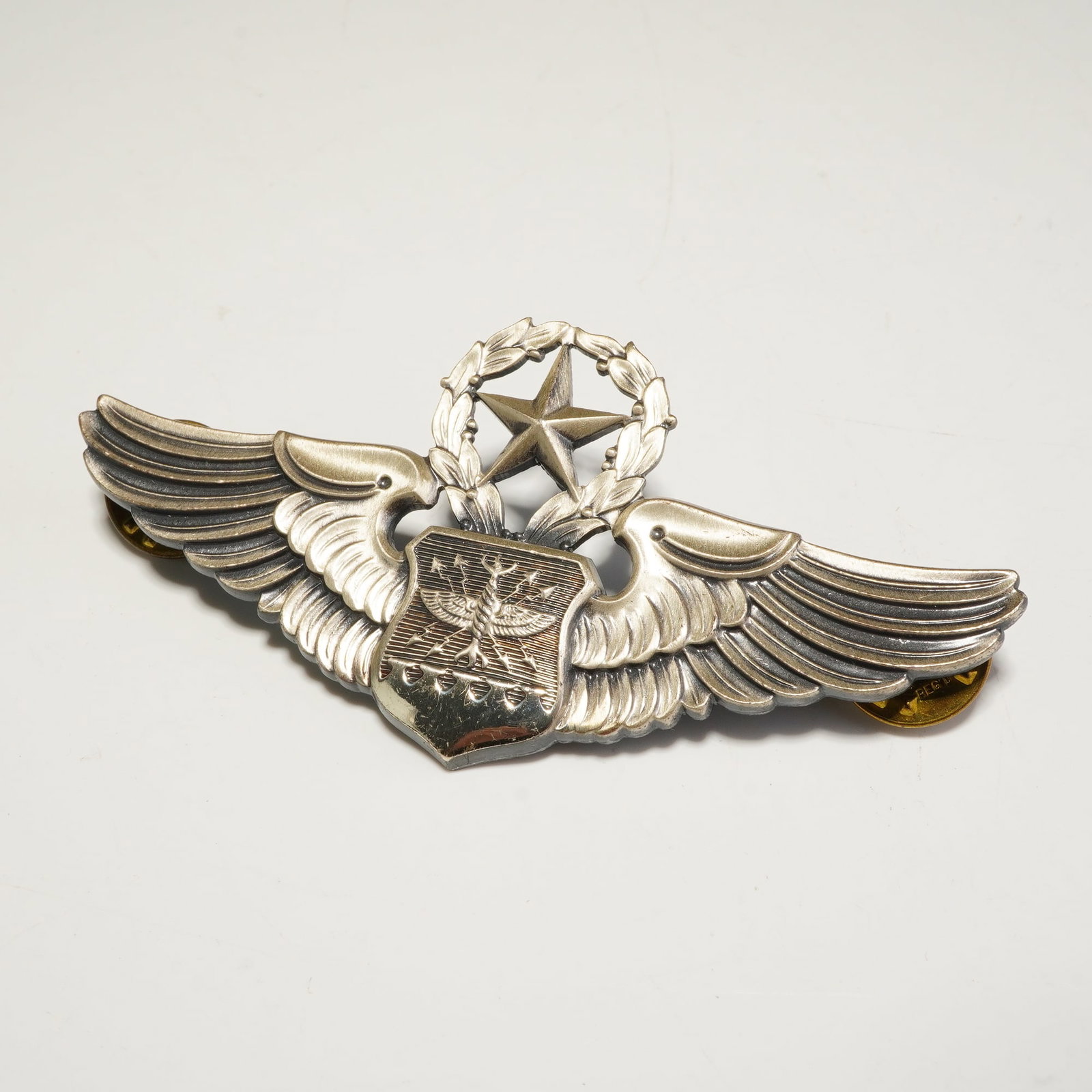 Sterling Silver U.S. Air Force Master Navigator Observer Badge: A United States Air Force Master Navigator / Observer badge crafted in sterling silver with a matte finish. The insignia features outspread wings flanking a central shield embossed with a wings and ar