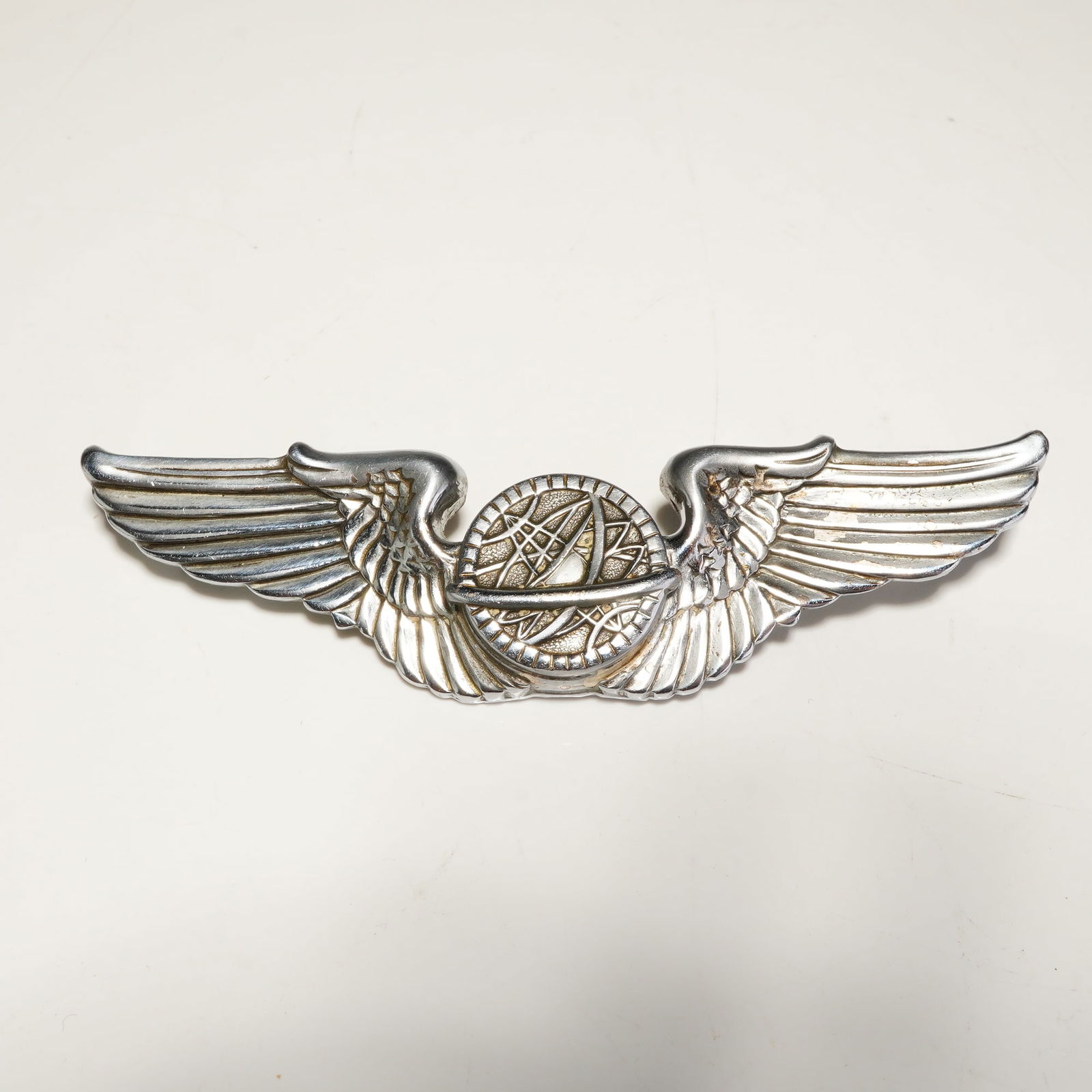 Sterling WWII U.S. Army Air Corps Navigator Wings Badge Pin: A WWII U.S. Army Air Corps navigator wings badge crafted from sterling silver. The insignia features a central circular emblem depicting a globe with meridians and an applied astrolabe, flanked by a p