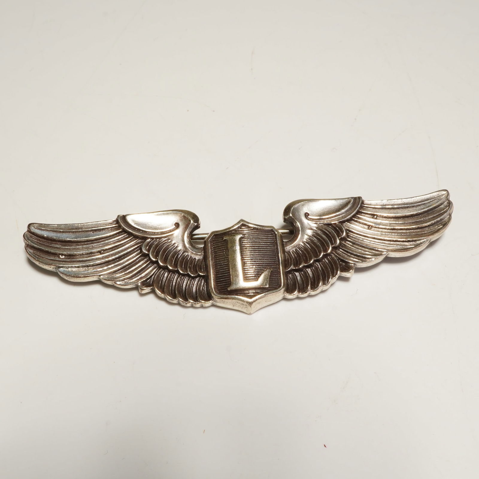 WWII AMICO Sterling U.S. Army Air Force Liaison Pilot Wings Badge: A World War II-era U.S. Army Air Force Liaison Pilot wings badge produced by the American Insignia Company (AMICO). The insignia is crafted from sterling silver and features a central shield embossed