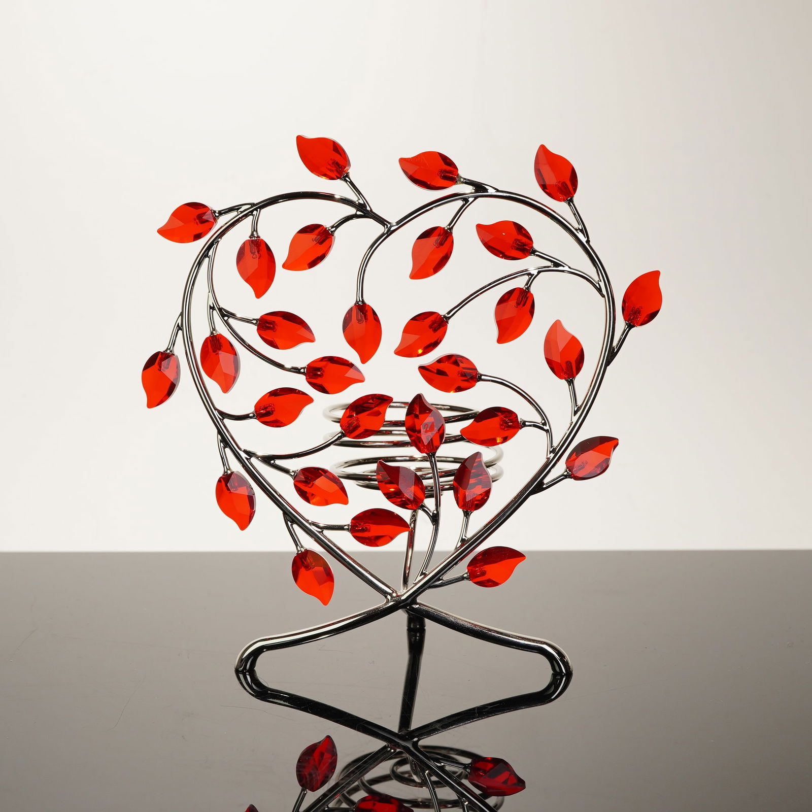 Silver-Tone Metal Swarovski Crystal Leaves Heart Candle Holder: This silver-tone metal Swarovski crystal leaves candle holder, model 660729, is a contemporary decorative piece featuring a heart-shaped frame. The frame is constructed from polished metal rods in a s