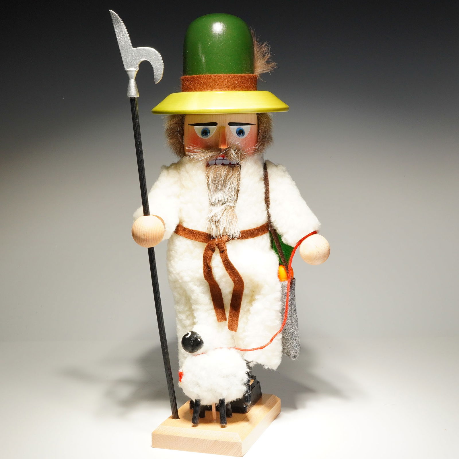 Steinbach Nutcracker, Shepherd: The figure is constructed from wood with hand-painted facial details and features a faux fur beard and hair. The shepherd is dressed in a white fleece robe secured with a brown cord belt and wears a g