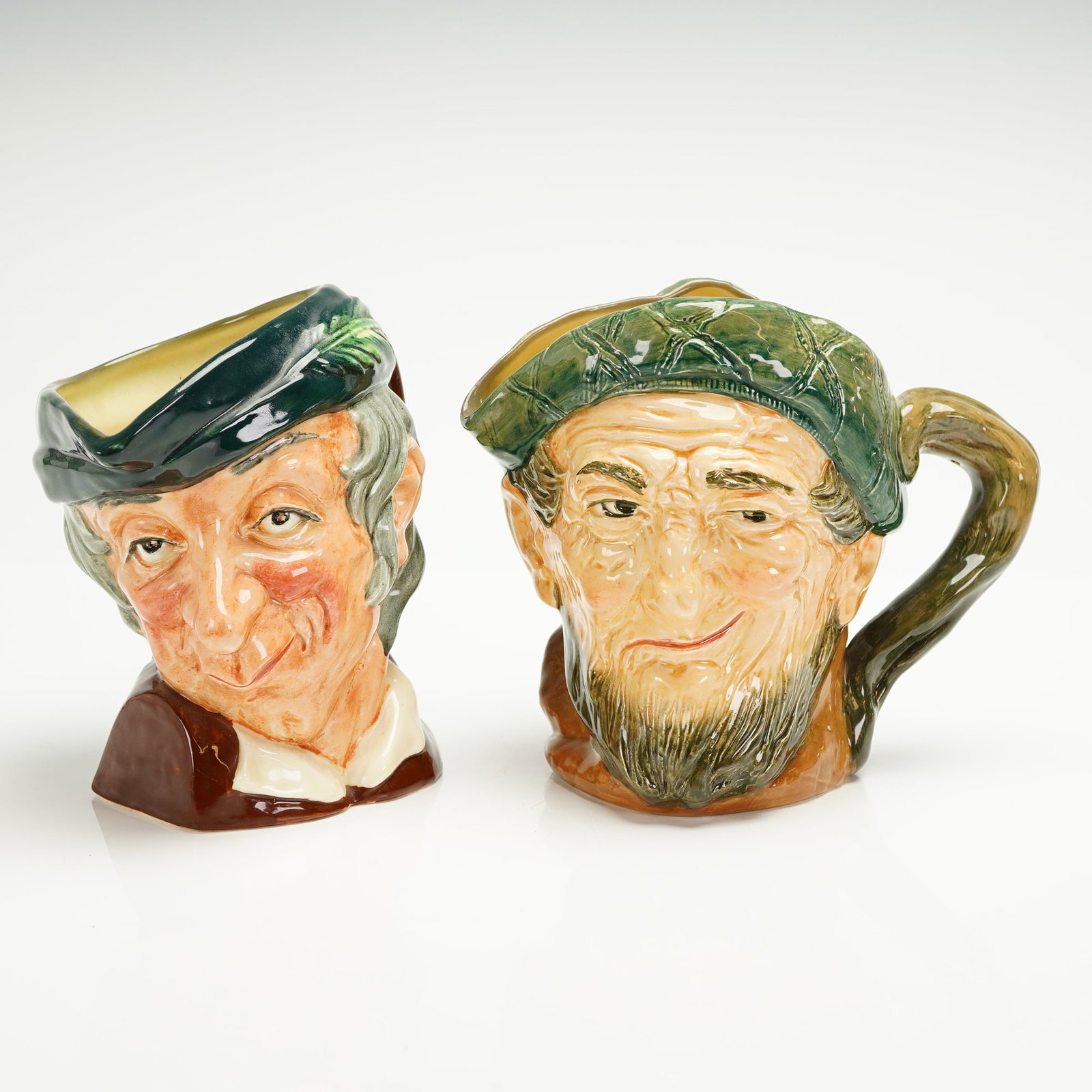 2pc Royal Doulton Large Character Jugs, Auld Mac and Simple Simon: A pair of vintage Royal Doulton polychrome glazed earthenware character jugs, identified as 'Auld Mac' (D5823) and 'Simple Simon' (D6374). Both jugs are executed in the style of miniature Toby jugs, f