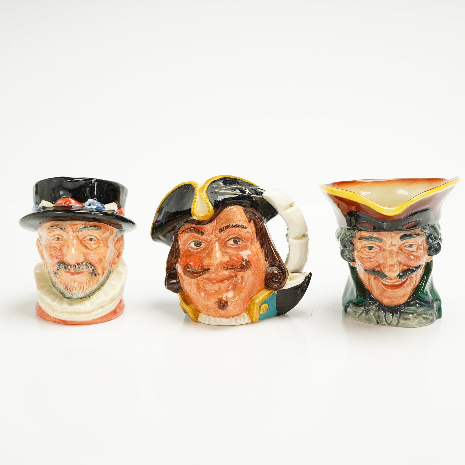 3pc Royal Doulton Small Character Jugs: A trio of Royal Doulton small Character Jugs, polychrome glazed ceramic, featuring highly detailed, hand-painted decoration and a high-gloss finish. The collection includes three distinct male charact