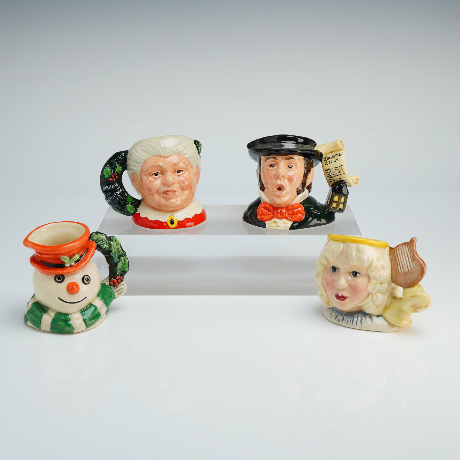 Set of 4 Royal Doulton Mini Character Jugs - D6922, D7007, D7051, & D7062: A set of four Royal Doulton miniature ceramic character jugs featuring festive holiday designs. Each piece is constructed of hand-painted ceramic finished with a high-gloss glaze. The group includes