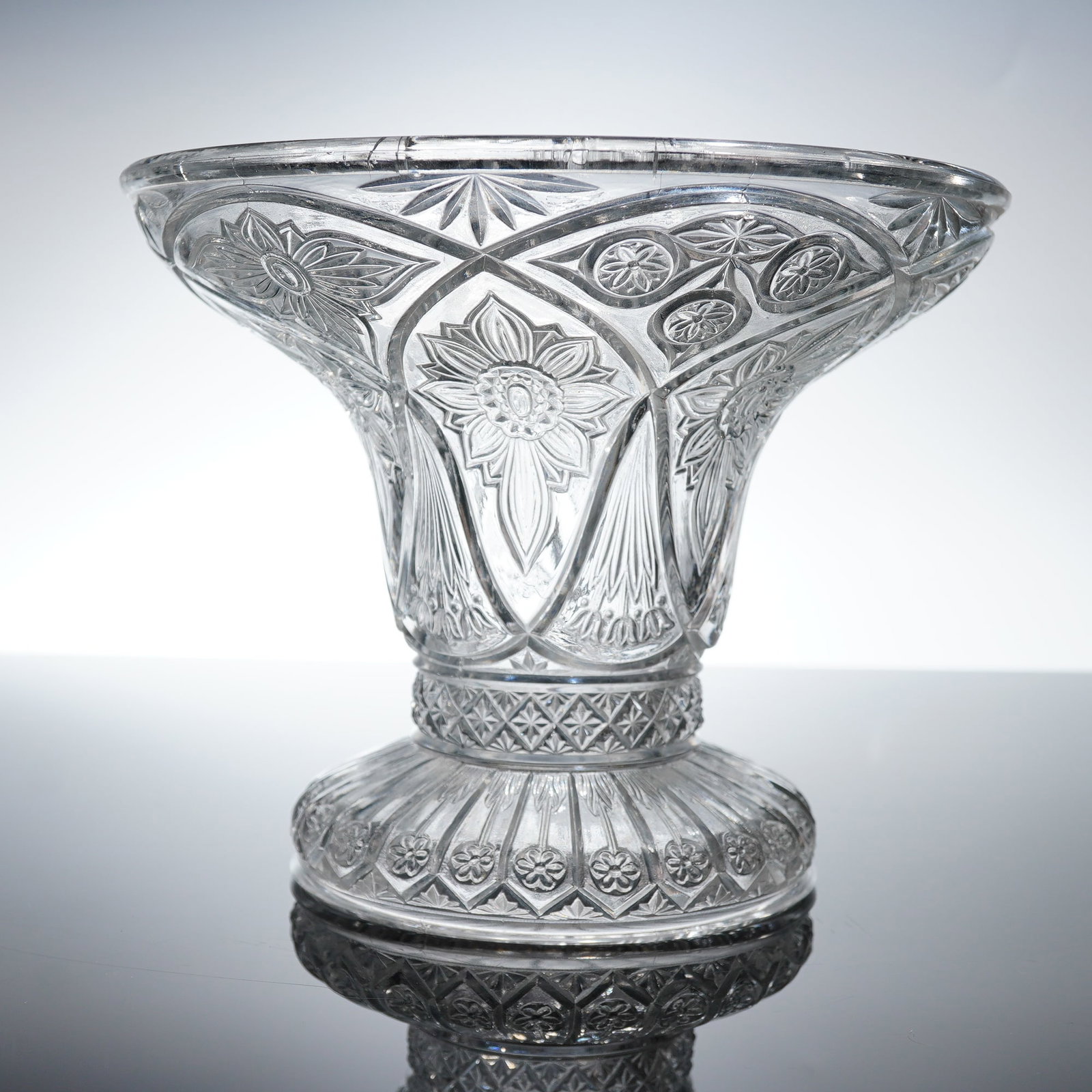 Early American Pressed Glass EAPG Footed Floral Vase: A single clear pressed glass footed vase executed in the Early American Pressed Glass (EAPG) style. The form features a trumpet-shaped body that rests upon a tiered, bulbous foot. The body is intensel