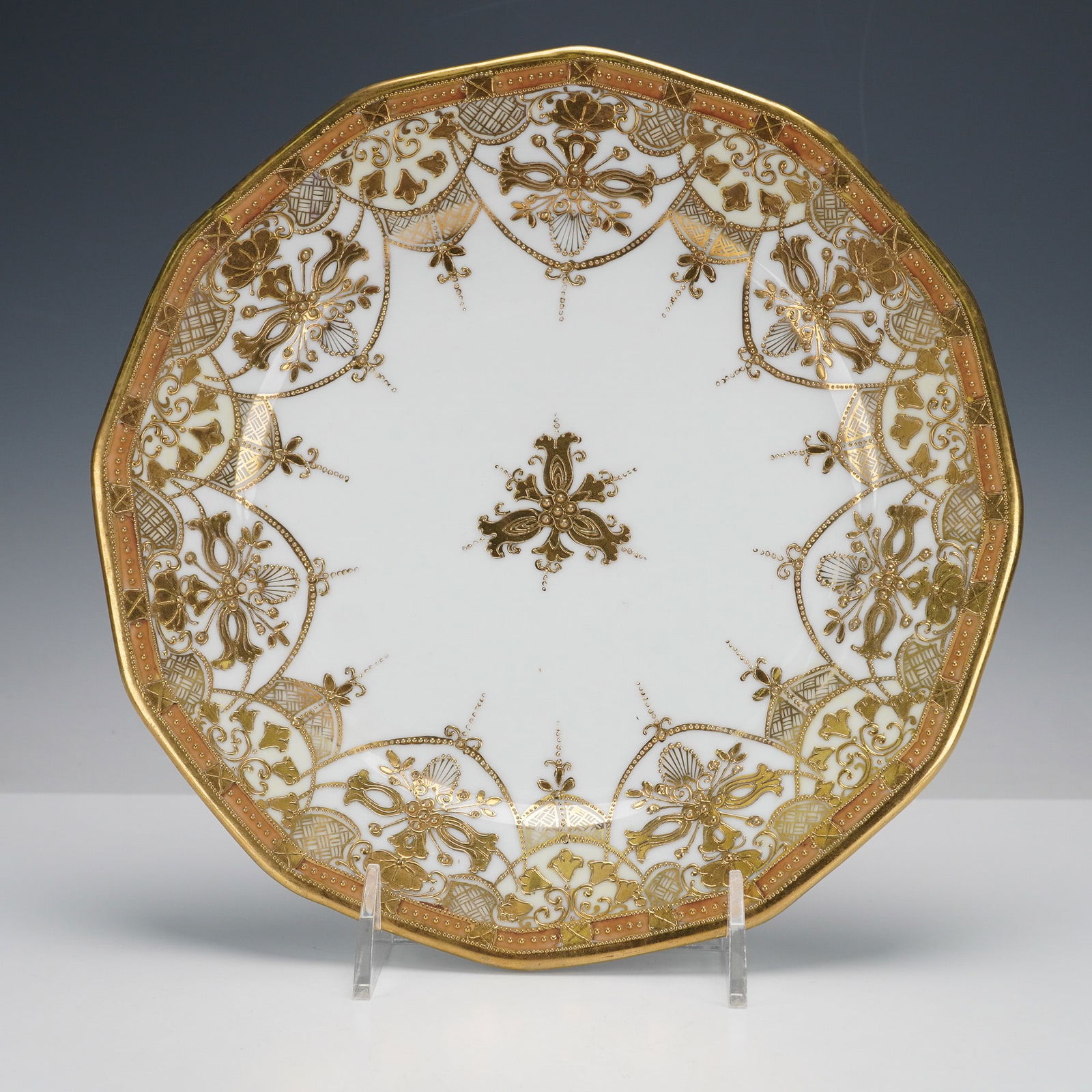 Nippon Hand Painted Raised Gold Octagonal Plate with RC Mark: A Nippon hand-painted raised gold octagonal plate that features an ornate, heavily gilded design against a white ground. A peachy-orange rim band is adorned with a fine lattice pattern in gold. The ce