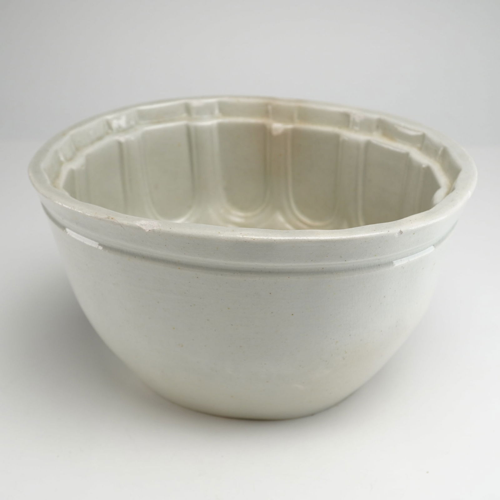 White Ironstone Pudding or Jello Mold with Floral Relief: The object is a single, antique Jello or Pudding Mold Pottery, likely Ironstone or heavy earthenware, characterized by its thick, bowl-shaped form and off-white/cream glaze. This utilitarian ceramic m