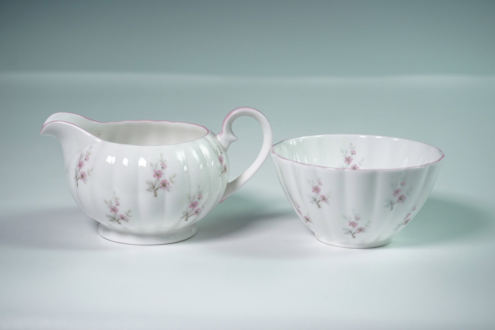 2pc Royal Tuscan Cream and Sugar Set, Pink Floral: Delicate bone china cream and sugar set by Royal Tuscan, featuring fluted white bodies adorned with petite pink floral sprays and soft pink trim. Both pieces are marked Royal Tuscan Fine Bone China,