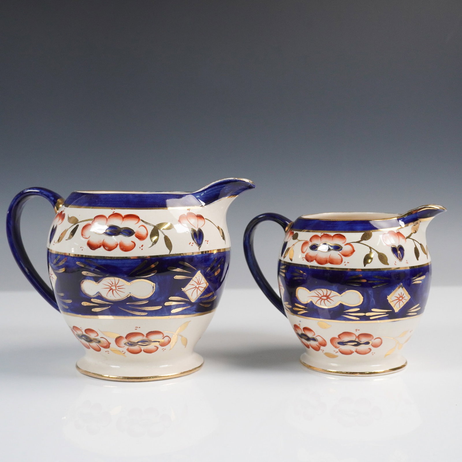 2pc Sadler Pitchers, Cobalt Blue with Floral and Gilt Detail: Charming 2-piece set of Sadler pitchers made in England, showcasing rich cobalt blue bands accented by hand-painted floral motifs and gilt detailing. These vintage earthenware pieces feature gracefull