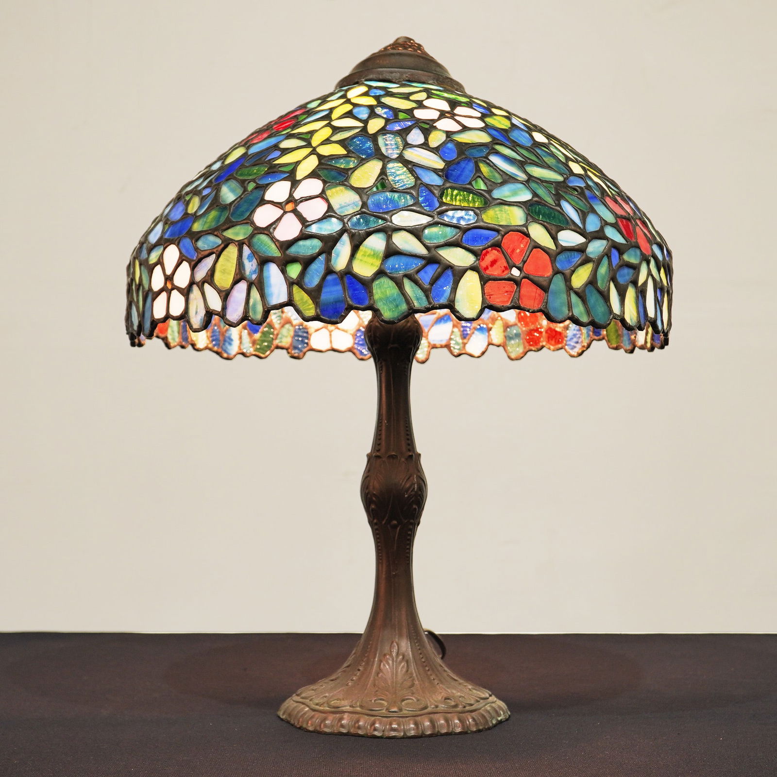 Tiffany Style Floral Stained Glass Table Lamp: This Tiffany inspired table lamp features a domed leaded glass shade decorated with a dense floral pattern. The design incorporates red, pink, yellow, and blue blossoms set against a green and blue