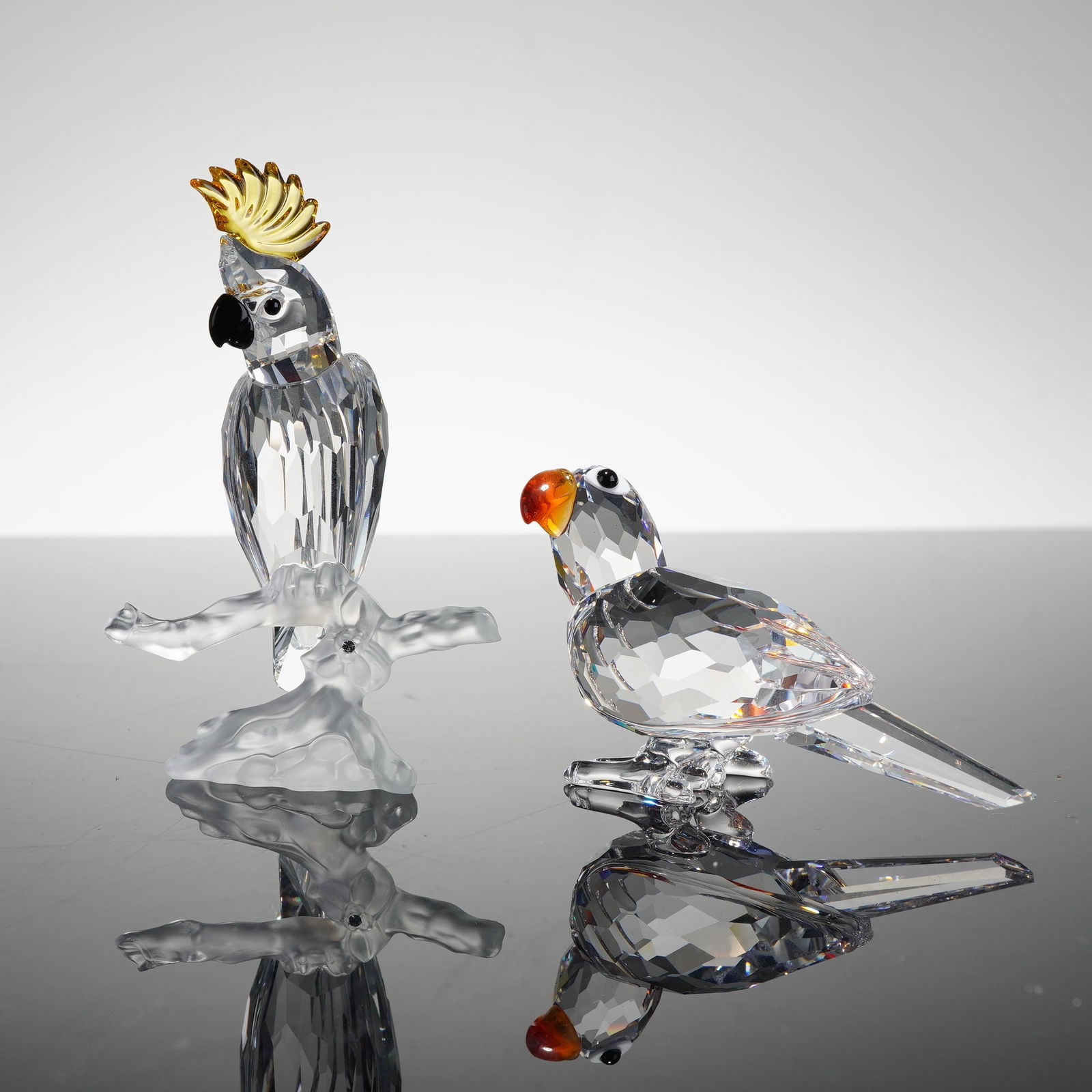 Swarovski Cockatoo 261635 and Parrot 294047 Figurines: A pair of Swarovski Silver Crystal bird figurines. The first is a Cockatoo, model number 261635, featuring a multifaceted clear crystal body, a yellow-amber crystal crest, and a black crystal beak and