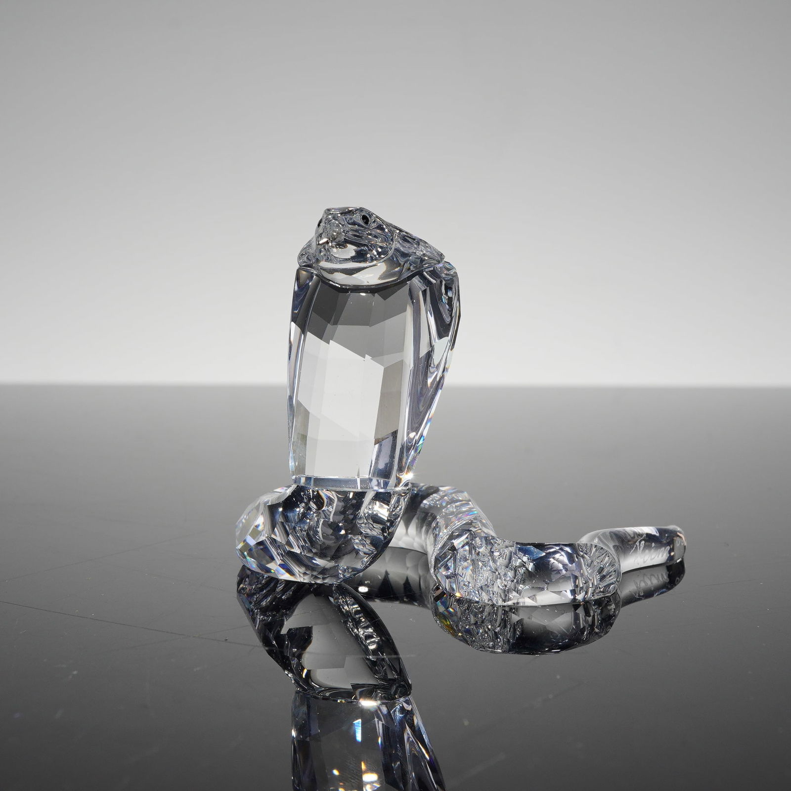 Swarovski Crystal Figurine Cobra Snake 243979: This Swarovski Silver Crystal figurine depicts a cobra in a dynamic striking pose with a flared hood and coiled body. Part of the African Wildlife collection, the piece is crafted from full lead facet