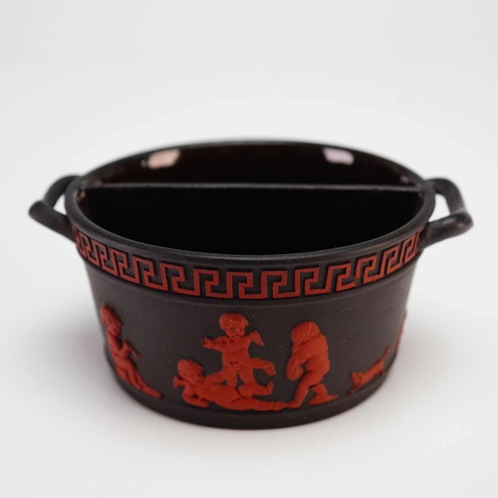Wedgwood Black Basalt and Rosso Antico Divided Salt Cellar: A Wedgwood dry-bodied stoneware divided salt cellar dating to approximately 1800. The ceramic vessel features a matte black basalt body with applied rosso antico red stoneware bas-relief decorations.