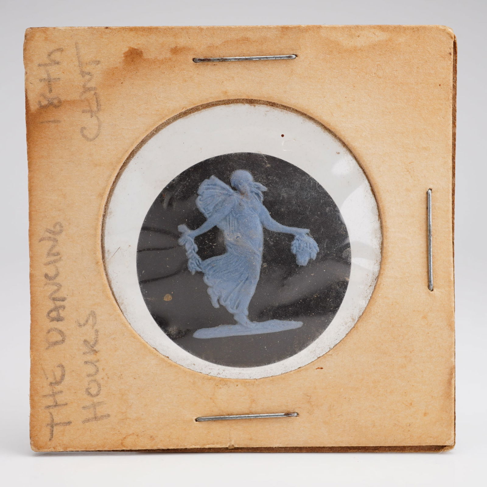 Wedgwood Black and Blue Jasperware Mini Plaque of the Dancing Hours: Circular black and blue Jasperware plaque depicting classical dancing figures. Retained in the original cardboard sheath labeled "The Dancing Hours" and "18th Century." The reverse is marked "Wedgwood