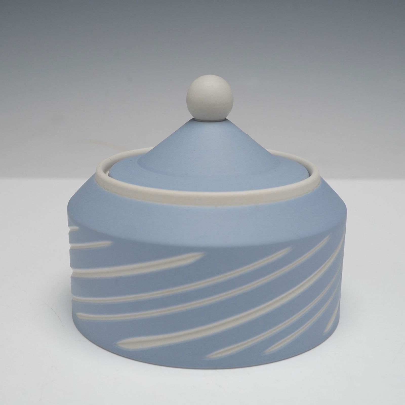 Wedgwood Pale Blue Jasperware Sugar Bowl with Lid: A Wedgwood pale blue jasperware covered sugar bowl. Crafted from matte stoneware, the exterior features a light powder blue finish with contrasting raised off-white/cream diagonal lines. The interior
