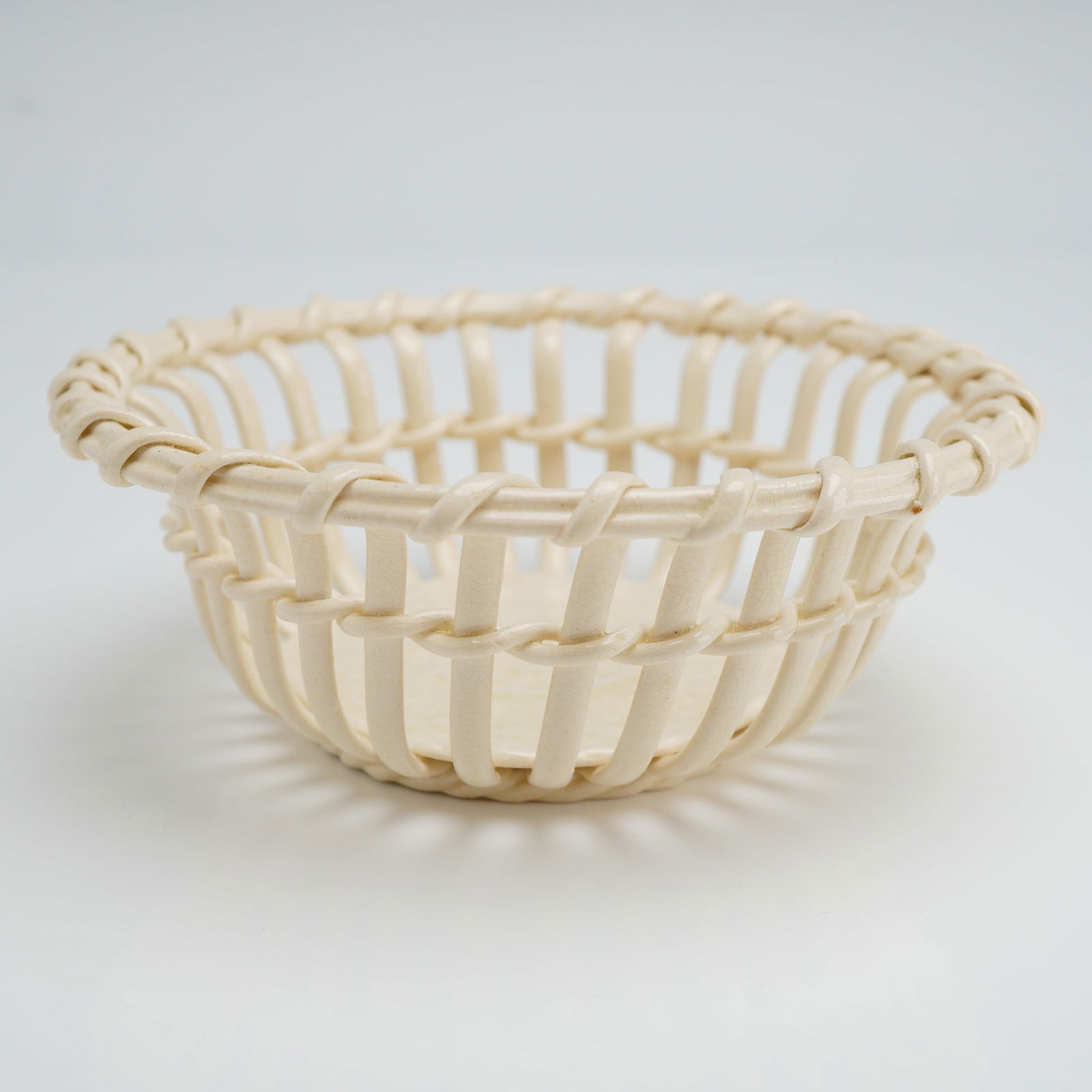 Wedgwood Creamware Lattice Basket: A Wedgwood creamware basket featuring intricate lattice-work and reticulated designs. The piece is crafted with a cream-glazed openwork body and a solid circular base. The construction incorporates a