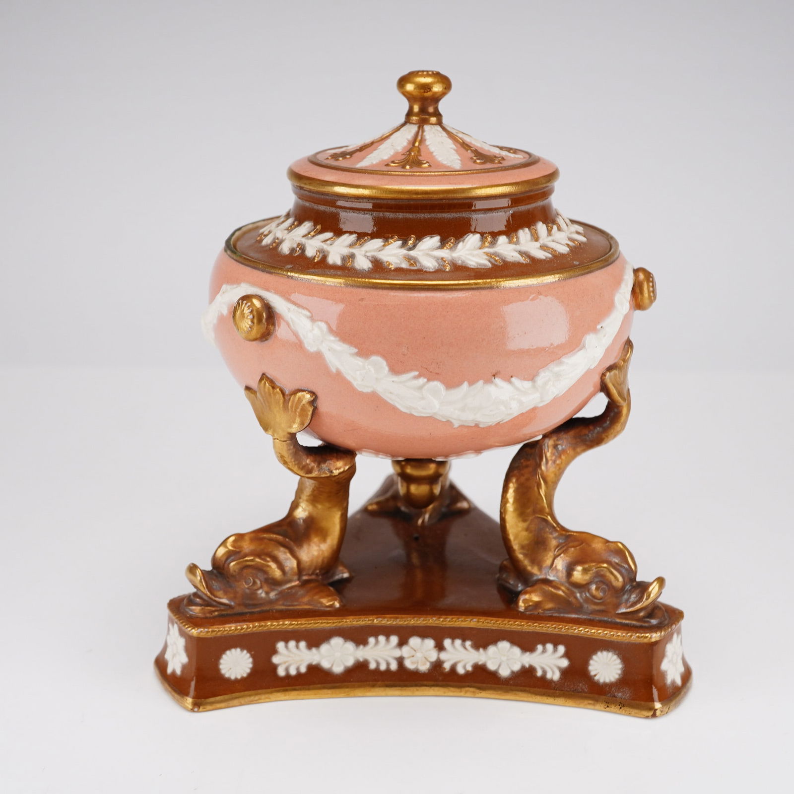 A Wedgwood Victoria Ware Covered Vase: A Wedgwood Victoria Ware covered vase, England, circa 1880. This Neoclassical style ceramic urn features a pink body decorated with white relief-molded floral swags and a pastille border. The vessel i