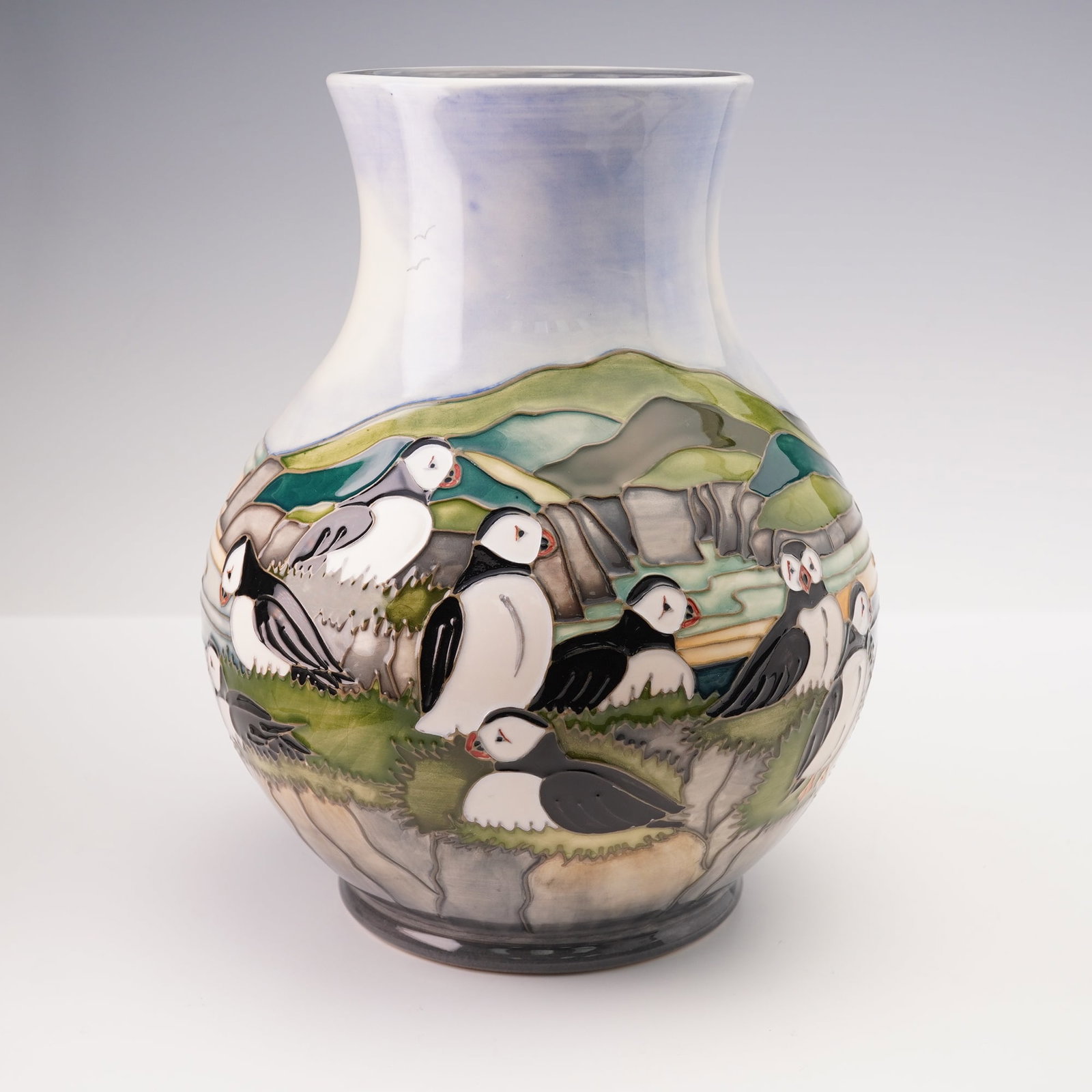 Moorcroft Pottery by Paul Hilditch Vase Puffins: A large bulbous shaped vase, painted by Paul Hilditch. It is decorated in tube lined technique with a continuous coastal scene of puffins nesting among rocky outcrops and grassy ledges. The birds pain
