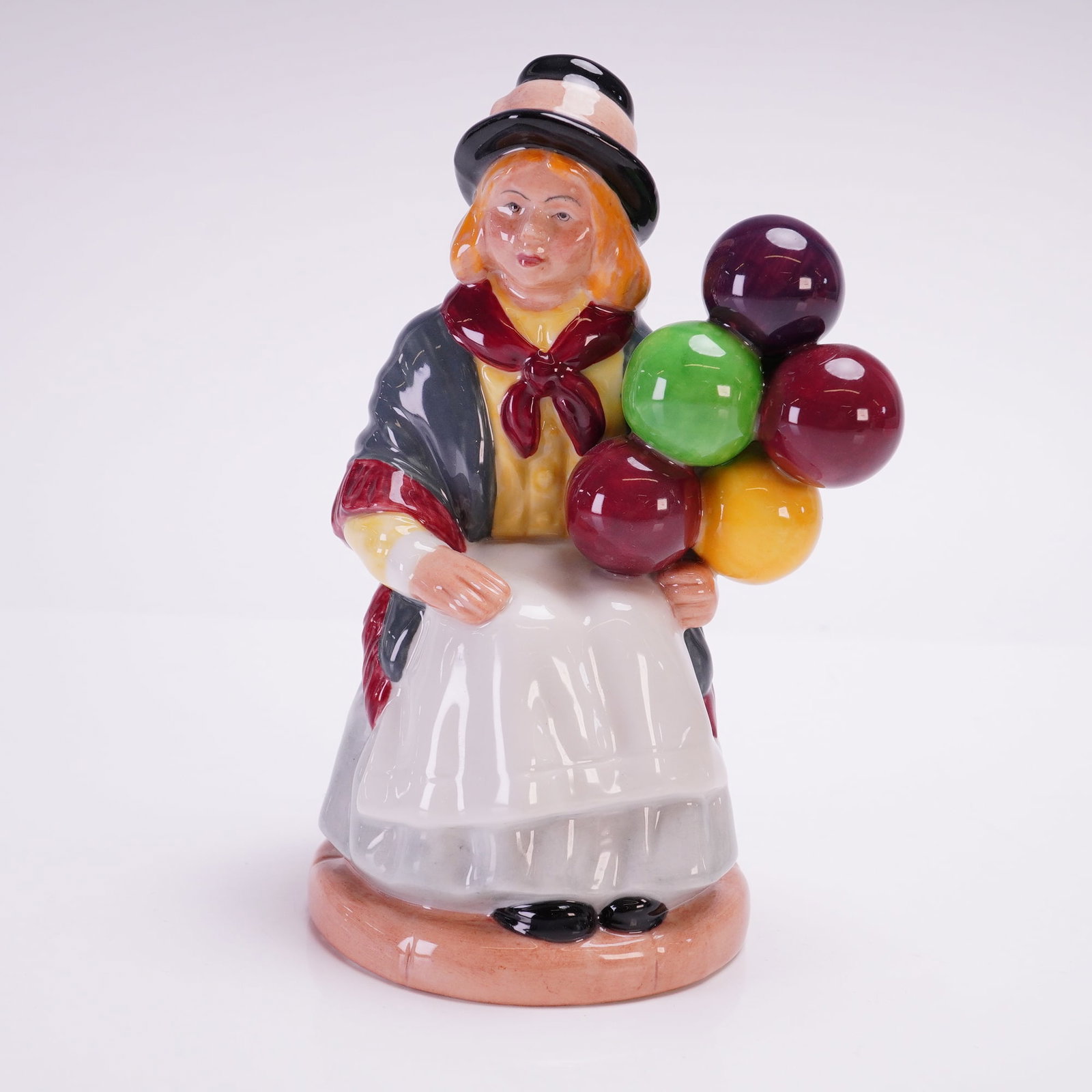 Royal Doulton Figurine Balloon Girl HN2818: Porcelain figurine designed by William K. Harper. The figure depicts a young girl in a bowler hat and shawl, seated with a colorful cluster of balloons in her hand. Finely hand-painted with vibrant gl