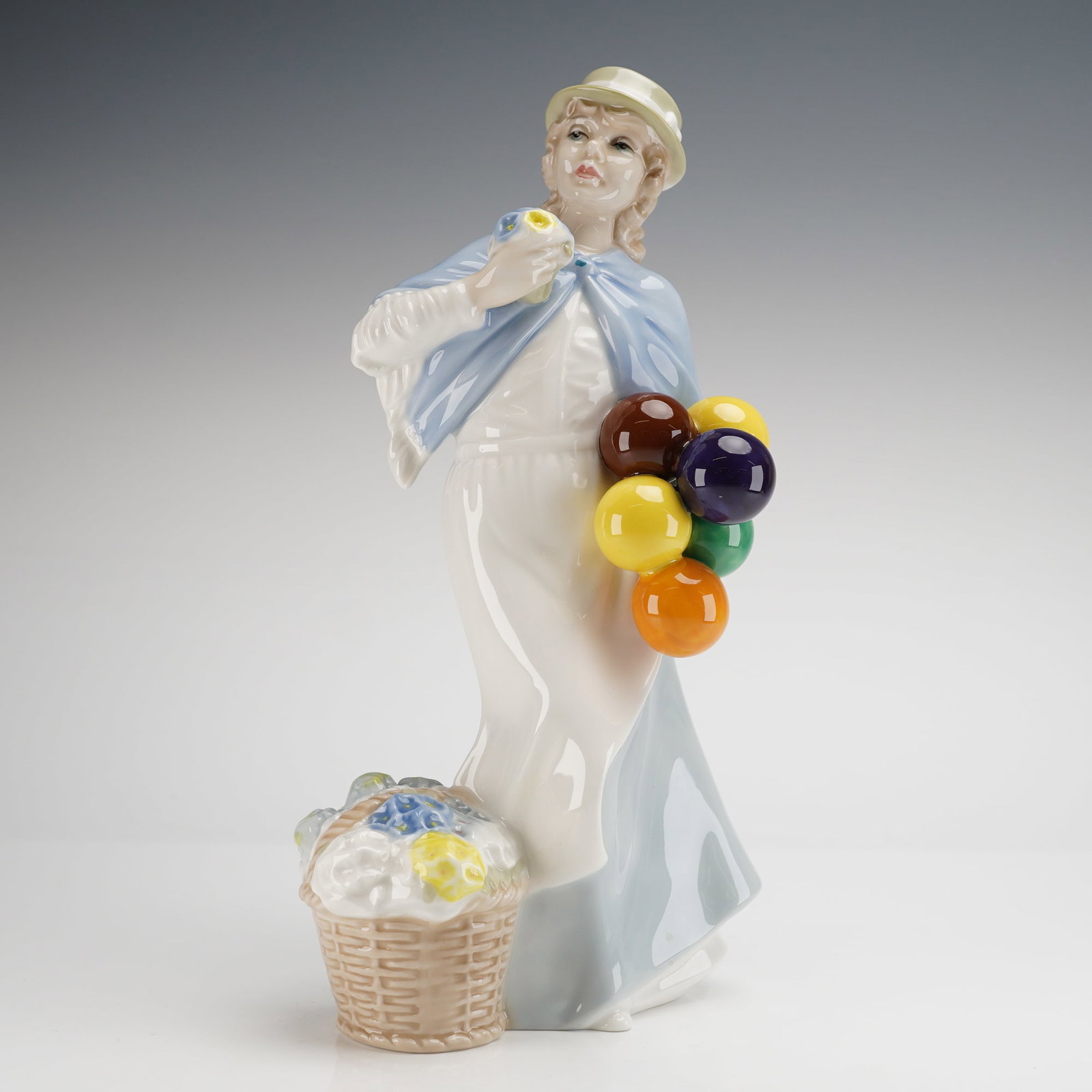 Royal Doulton Reflections Figurine Covent Garden HN2857: Depicts a female street vendor dressed in a long white and pale blue gown, complemented by a cream hat and shawl. She holds a small bouquet of yellow flowers and a cluster of brightly colored balloons