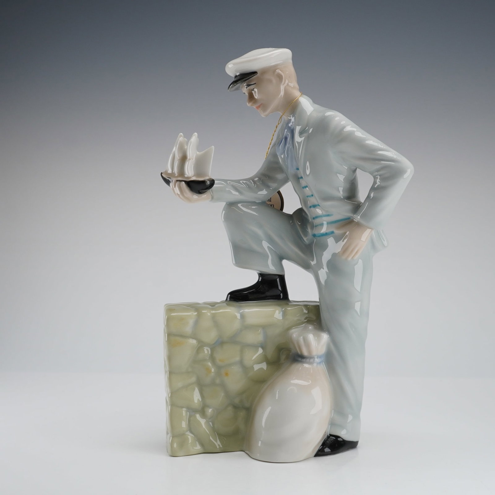 Royal Doulton Figurine Traveller's Tale HN3185: The piece, part of the Reflections Series and modelled by Eric J. Griffiths and dated 1987, depicts a young man in a light blue suit and white peaked cap, kneeling with one foot resting on a textured