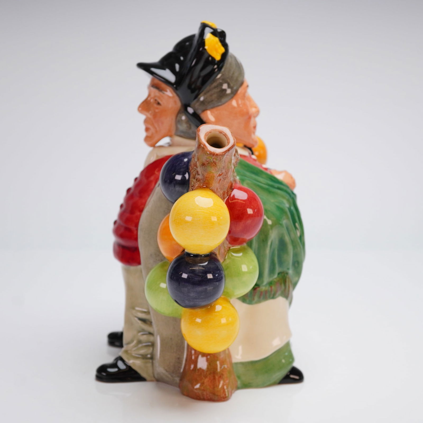 Royal Doulton Lidded Teapot Balloon Man / Balloon Woman D7171: This double character teapot is executed in polychrome glazed ceramic, depicting the Balloon Man (wearing a red waistcoat) and the Balloon Woman (wearing a green shawl) standing back-to-back. The figu