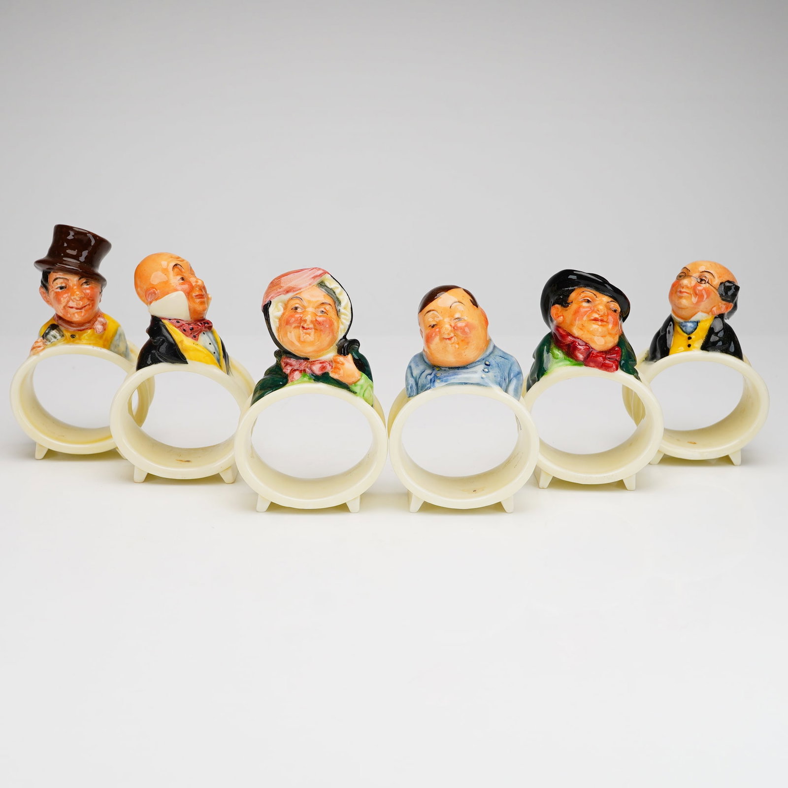 Set of 6 Royal Doulton Dickens Characters Napkin Rings: Each ring features a hand-painted polychrome bust of a character from the works of Charles Dickens, including Sam Weller, Micawber, Sairey Gamp, Fat Boy, Tony Weller, and Mr. Pickwick. The stylized fi