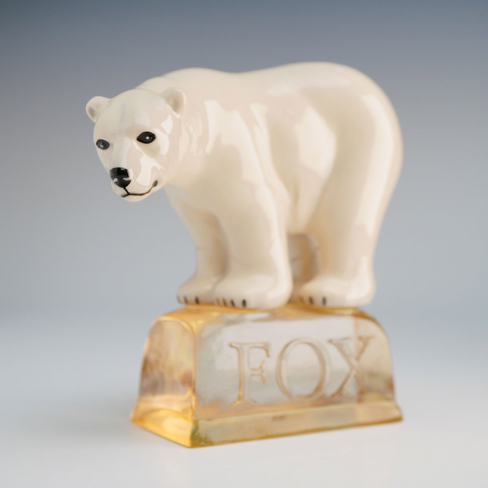 Royal Doulton 20th Century Advertising Figurine Fox's Polar Bear AC4: This porcelain figure is finished in a high-gloss white glaze with black painted details on the eyes, nose, and claws. The bear is depicted standing on a translucent, amber-toned base molded to resemb