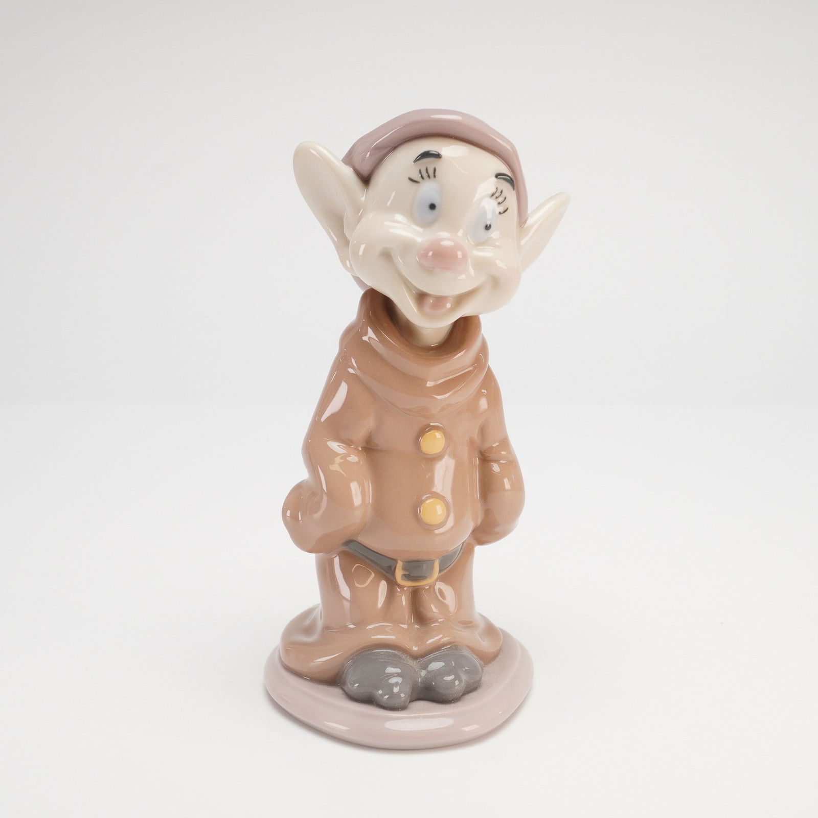 Lladro Dopey Dwarf Figurine #7534: A Lladro glossy porcelain figurine, model 7534, depicting the character Dopey from Disney's animated classic Snow White and the Seven Dwarfs. The figure is portrayed in a standing pose, wearing his si